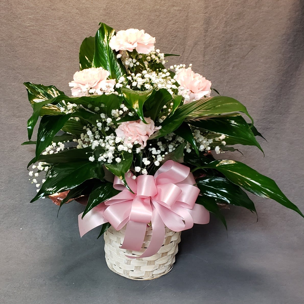 Pink carnations and baby's breath in a white basket with a pink ribbon