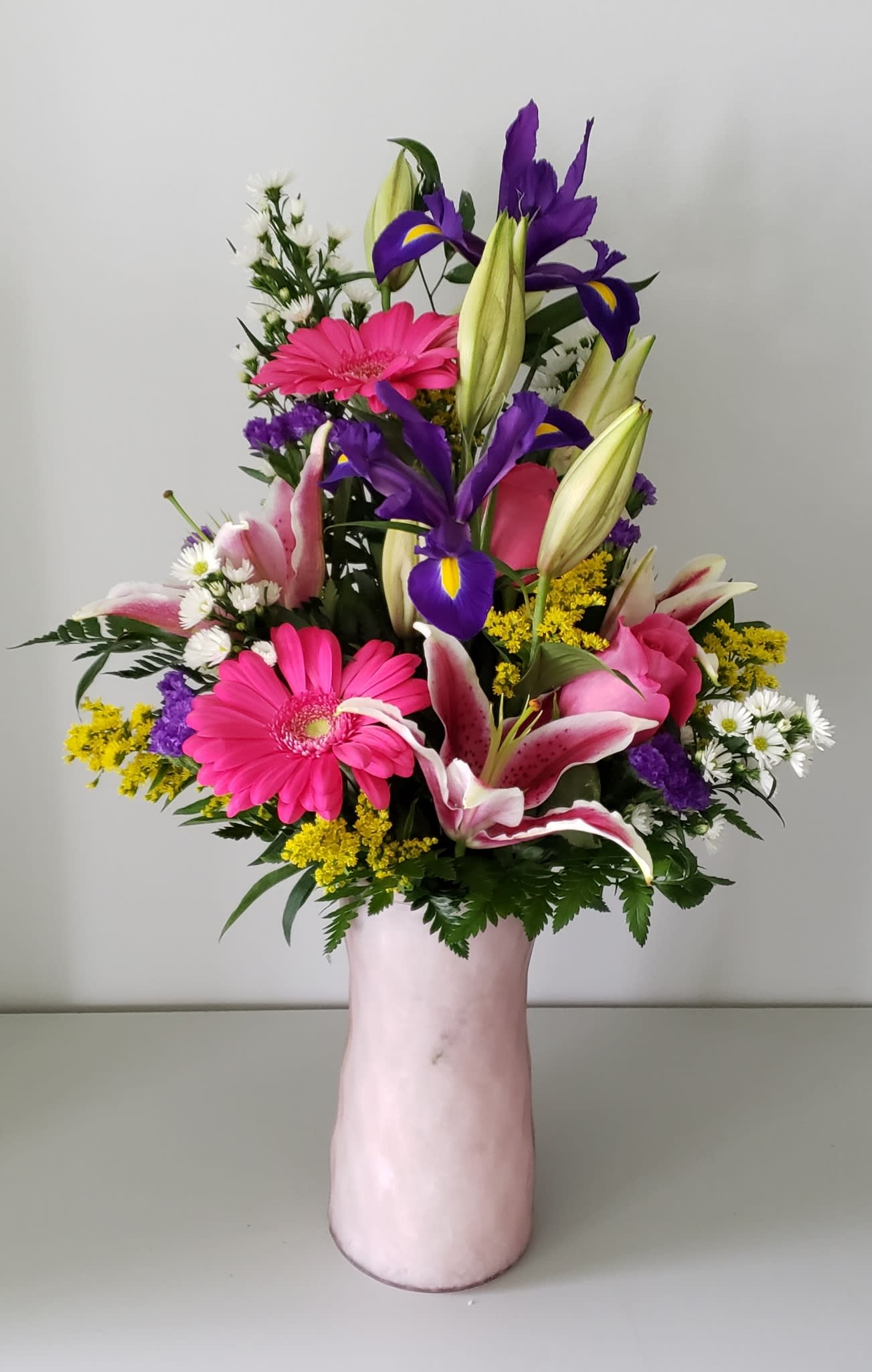 Mixed bouquet with pink gerberas, purple irises, and lilies in a pink vase