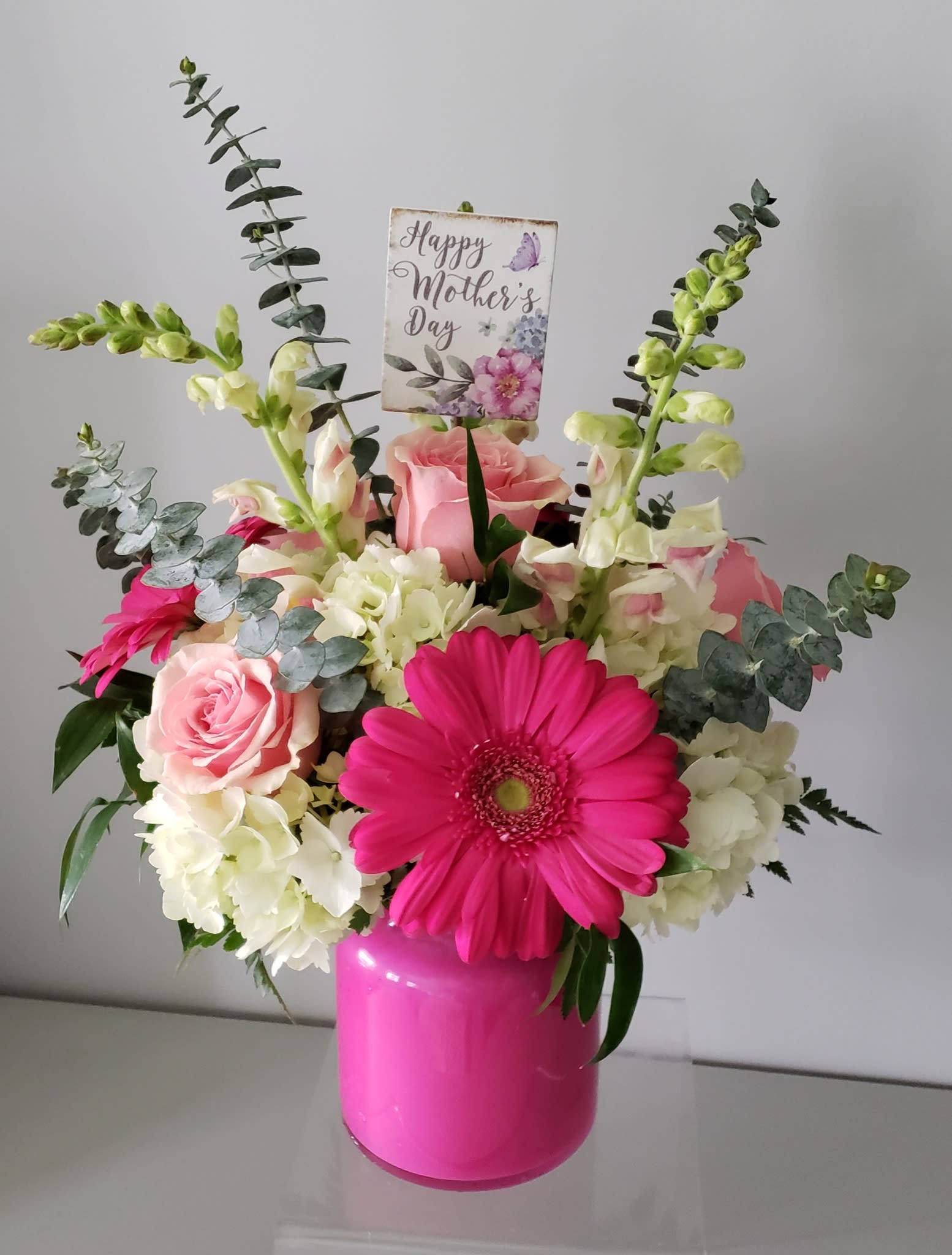 Pink and white floral arrangement in a bright pink vase with a Mother’s Day card