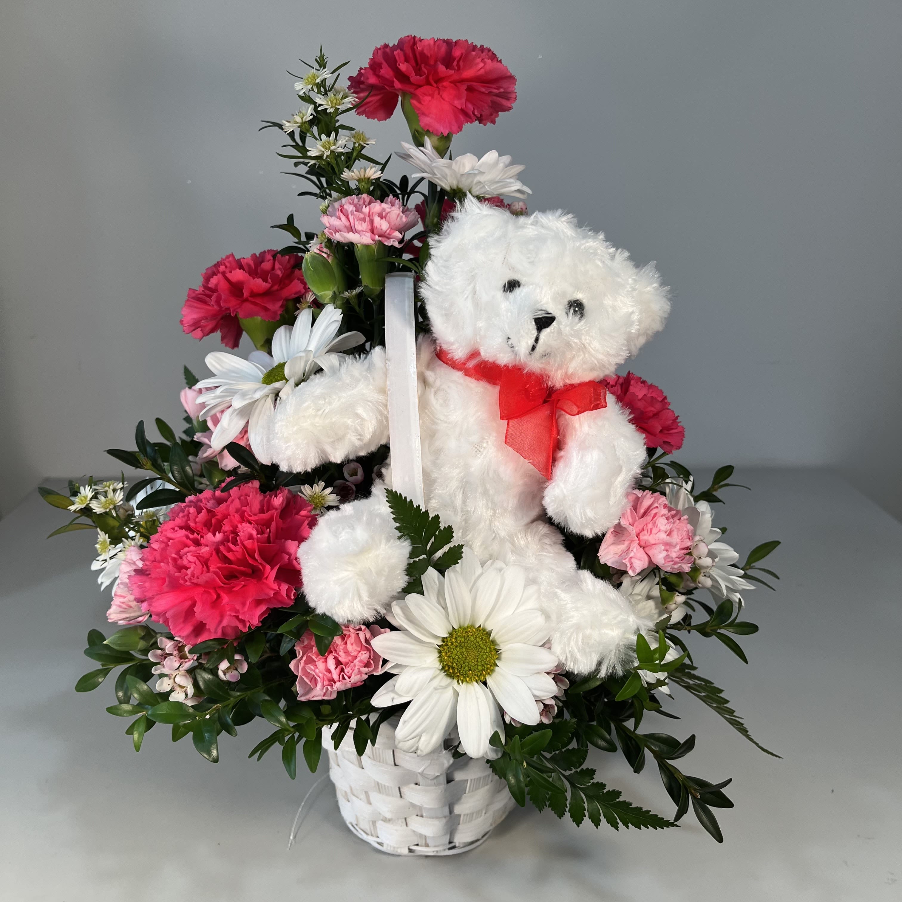 White teddy bear in a basket with pink and white flowers