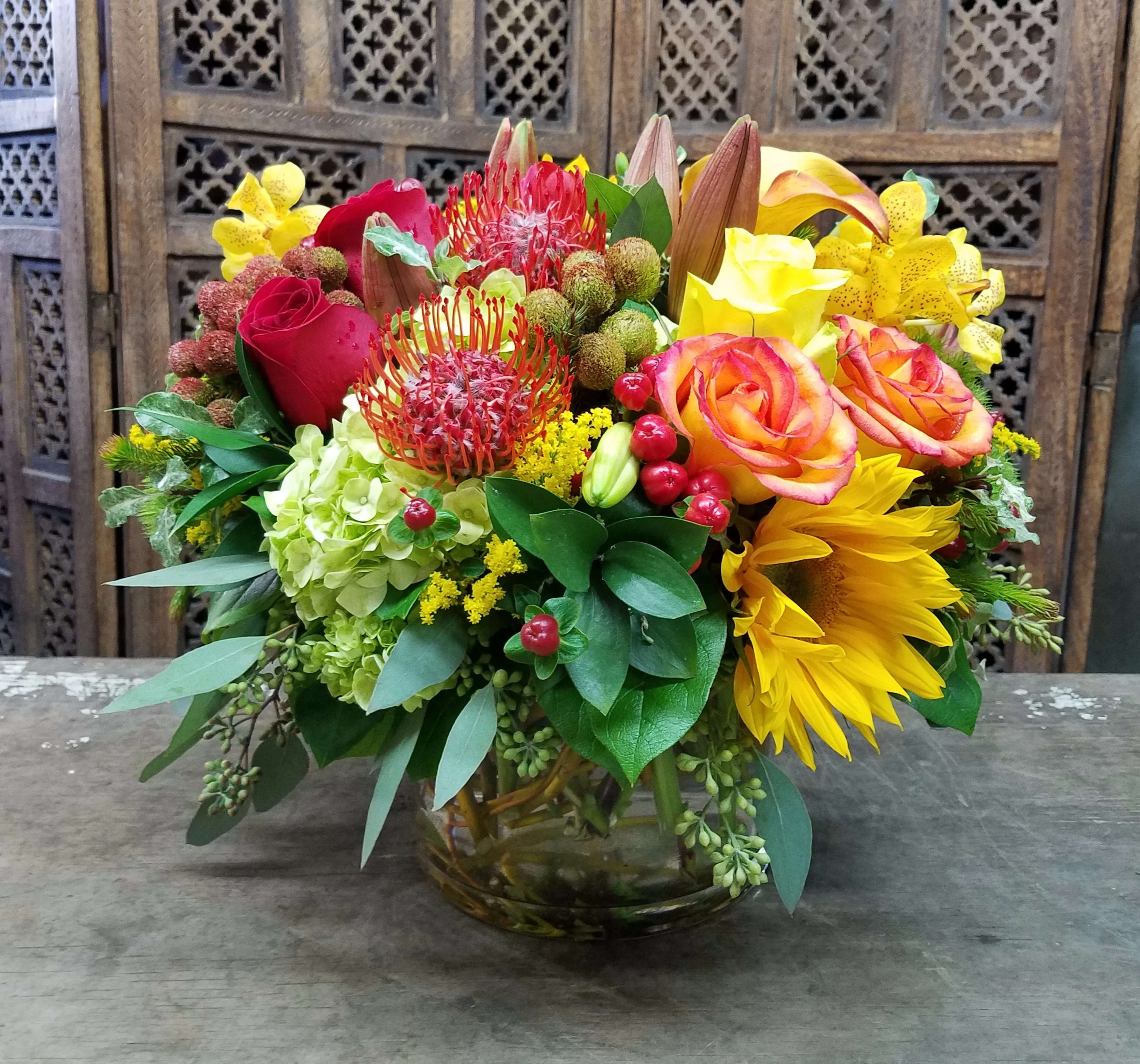 Mixed bouquet in a glass vase with roses, sunflowers, and orchids