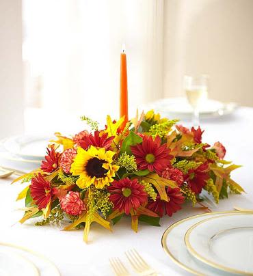 Fields of Europe Centerpiece - Inspired by the rich, colorful blooms found in the European countryside in autumn, our bestselling centerpiece is hand-arranged with fresh roses, sunflowers, lilies, daisies and carnations. With touches of dried oak leaves and an orange taper candle, it's a welcome addition to family gatherings, housewarmings or as part of the fall dÃ©cor. Centerpiece arrangement of roses, sunflowers, lilies, daisy poms, mini carnations, solidago and salal, accented with dried oak leaves Lilies may arrive in bud form and will open to full beauty over the next 2-3 days Includes a 12"L orange taper candle (overall dimensions do not include candle) Large arrangement measures approximately 8"H x 17"L Medium arrangement measures approximately 7.5"H x 16"L Small arrangement does not include roses or lilies; measures approximately 6"H x 15"L Our florists hand-design each arrangement, so colors, varieties and container may vary due to local availability.