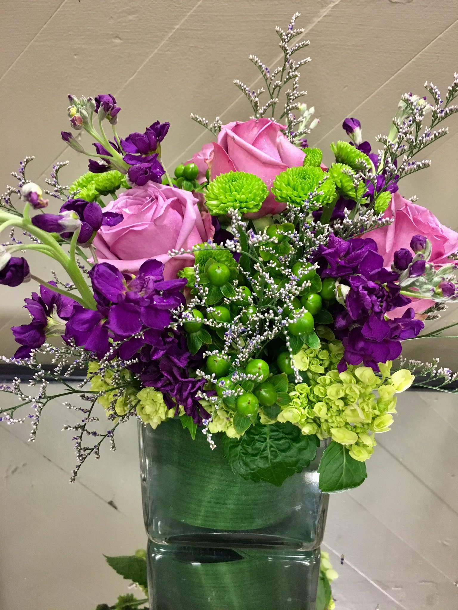 Pink roses and purple flowers arranged in a square glass vase