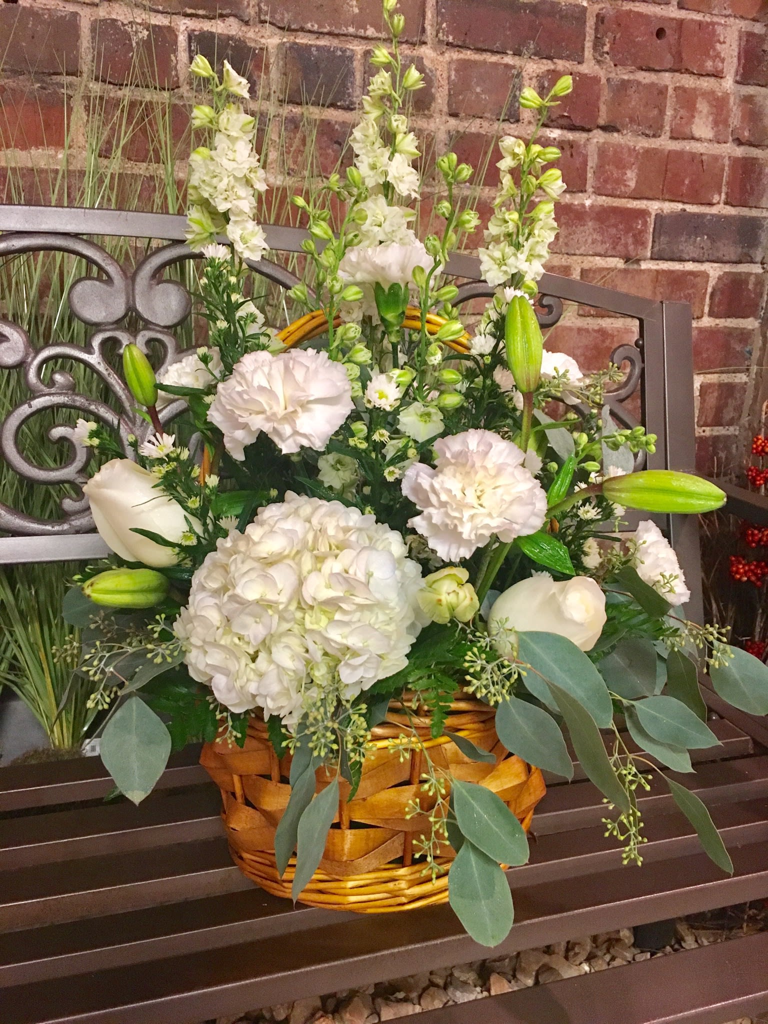 White floral arrangement in a wicker basket with lilies, hydrangea, and tall blooms