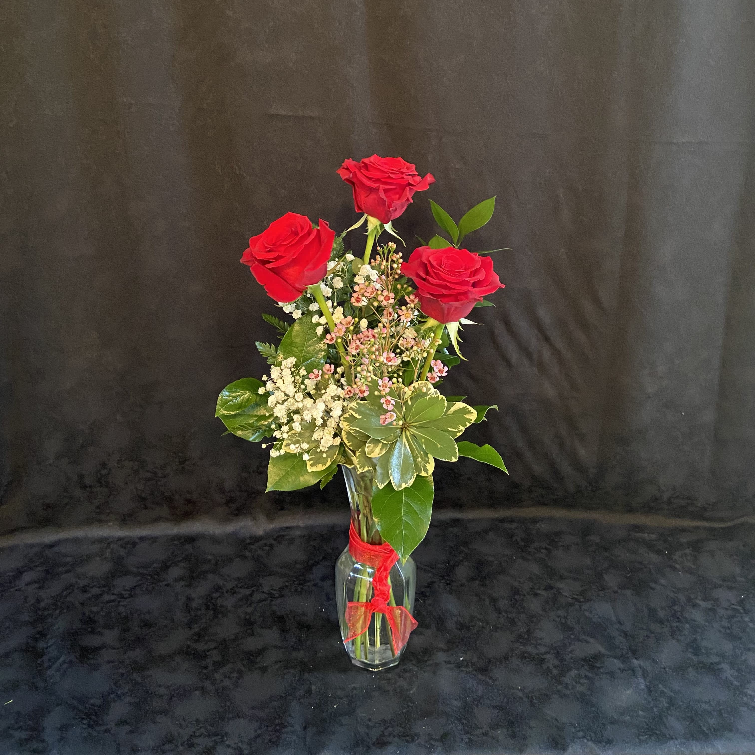 Three red roses in a clear glass vase with a red ribbon