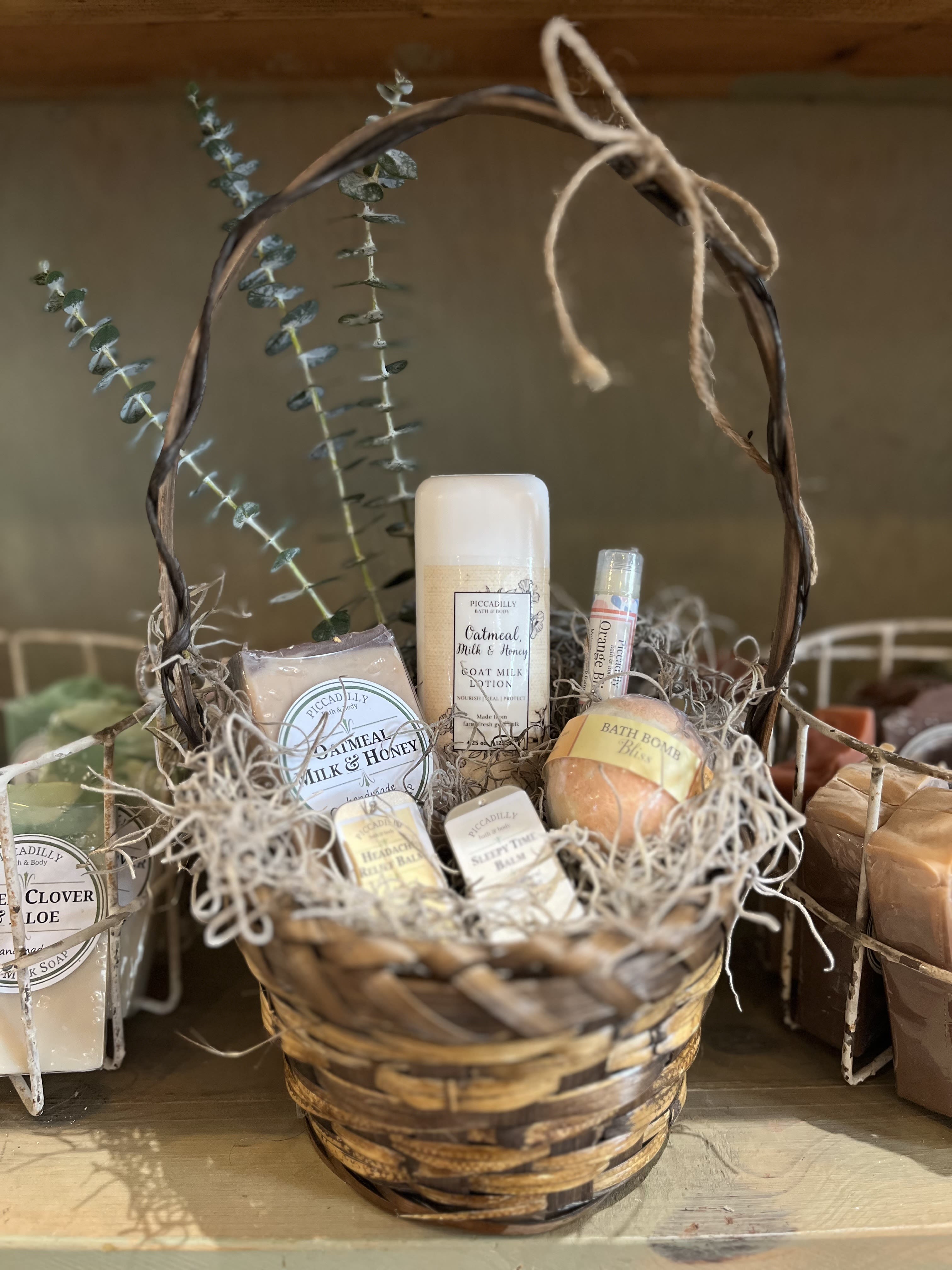 Spa Day - Includes locally made Piccadilly Bath and Body soap, lotion, bath bomb, headache and sleepy time balm and lip balm with a few sprigs of fresh eucalyptus in a wicker basket.