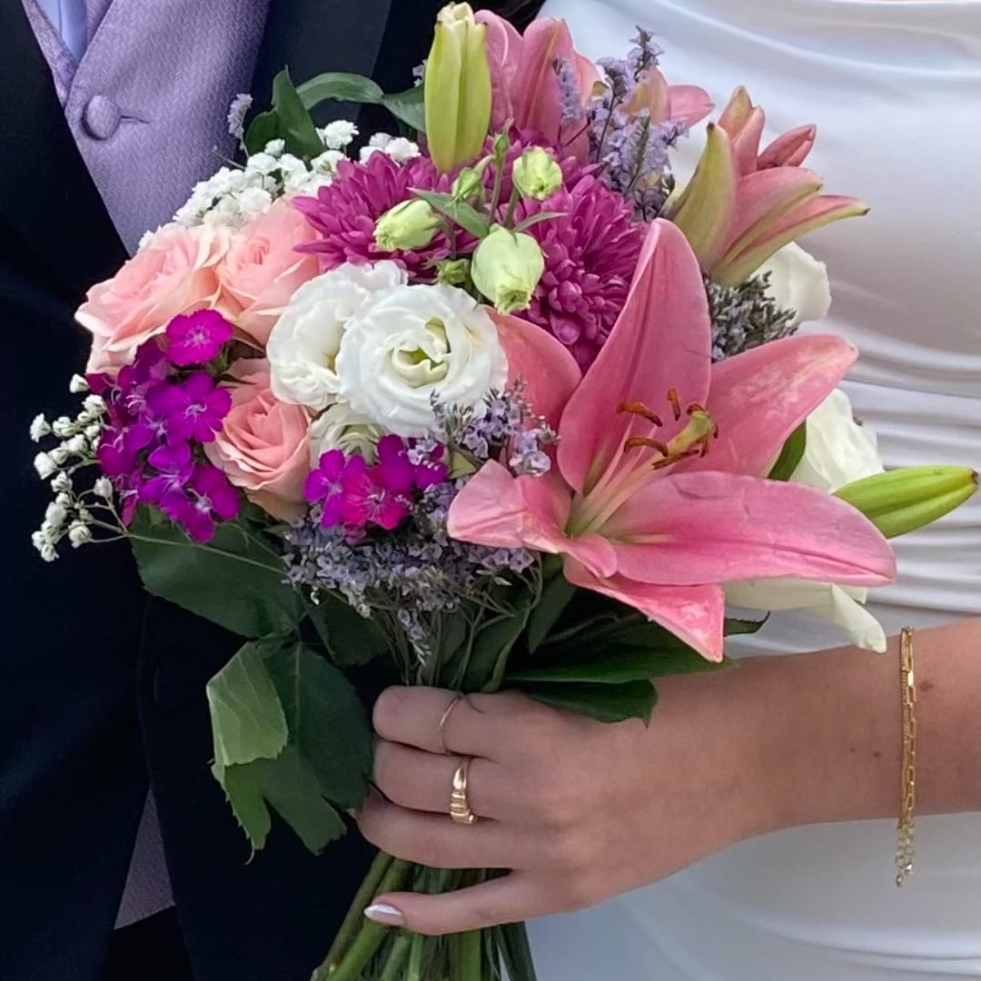 Handheld bouquet of pink lilies, roses, and white blooms