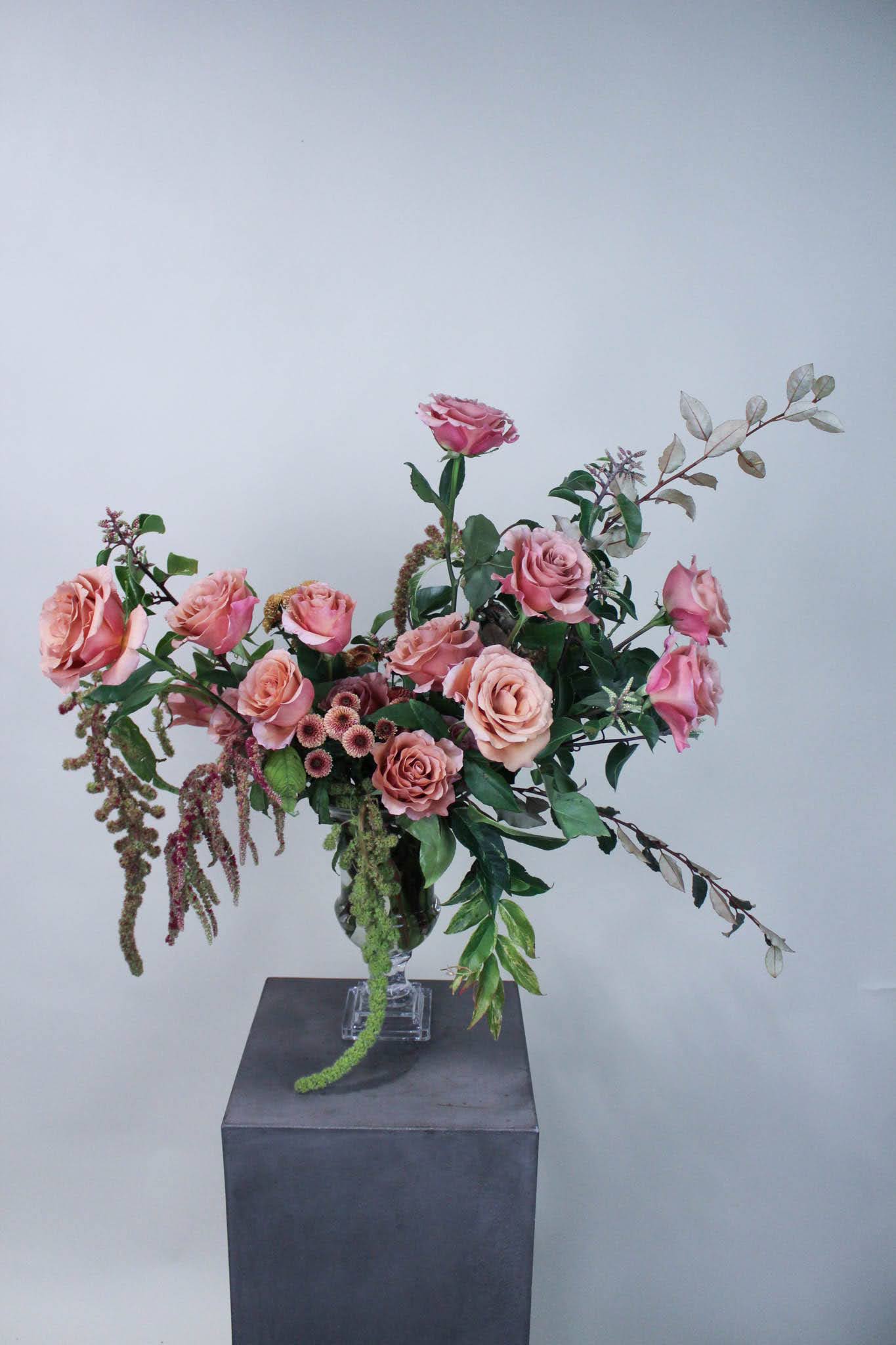 Pink roses arranged in a clear glass vase with trailing greenery