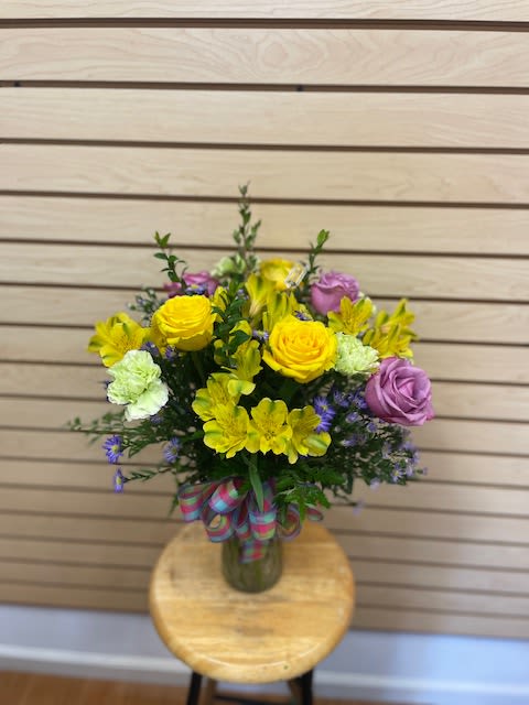Bouquet of yellow and lavender flowers in a glass vase with a ribbon