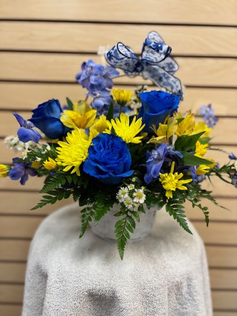 Blue roses and yellow daisies in a white vase with a patterned ribbon bow