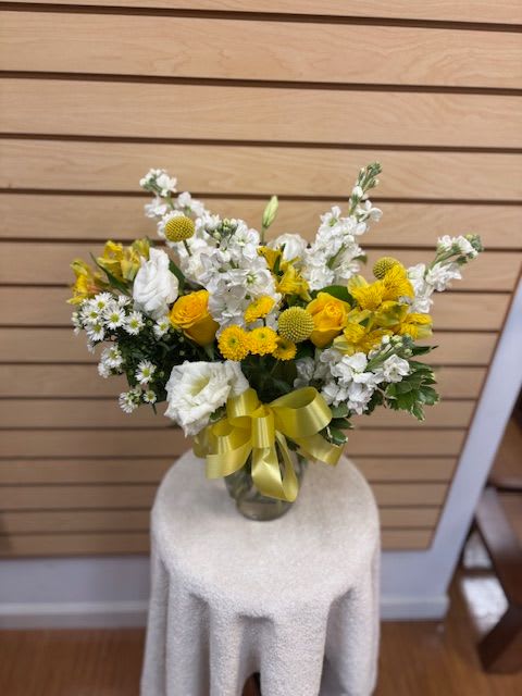 Yellow and white flower arrangement in a glass vase with a ribbon