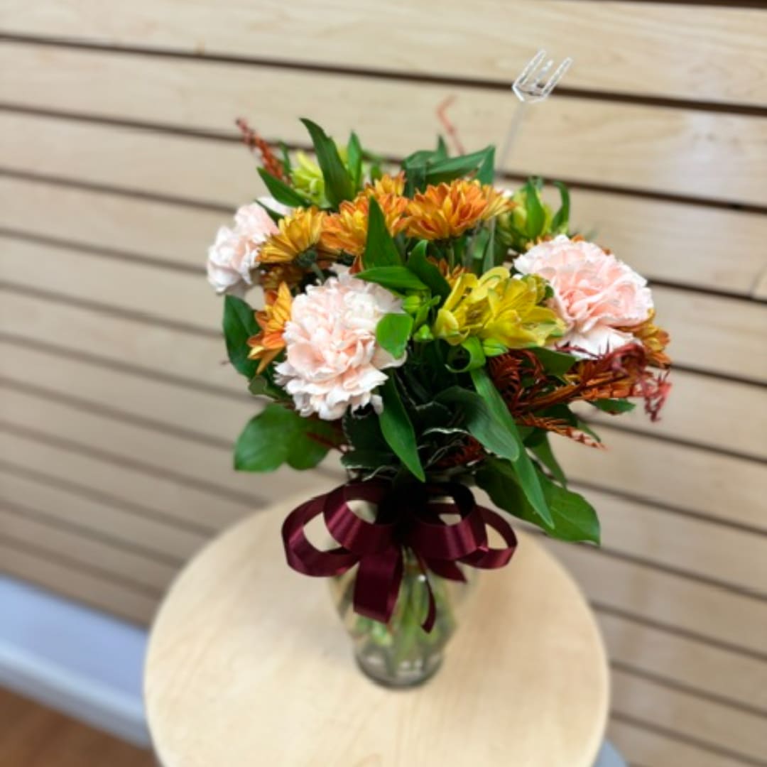 Bouquet of peach carnations and orange flowers in a glass vase with a ribbon