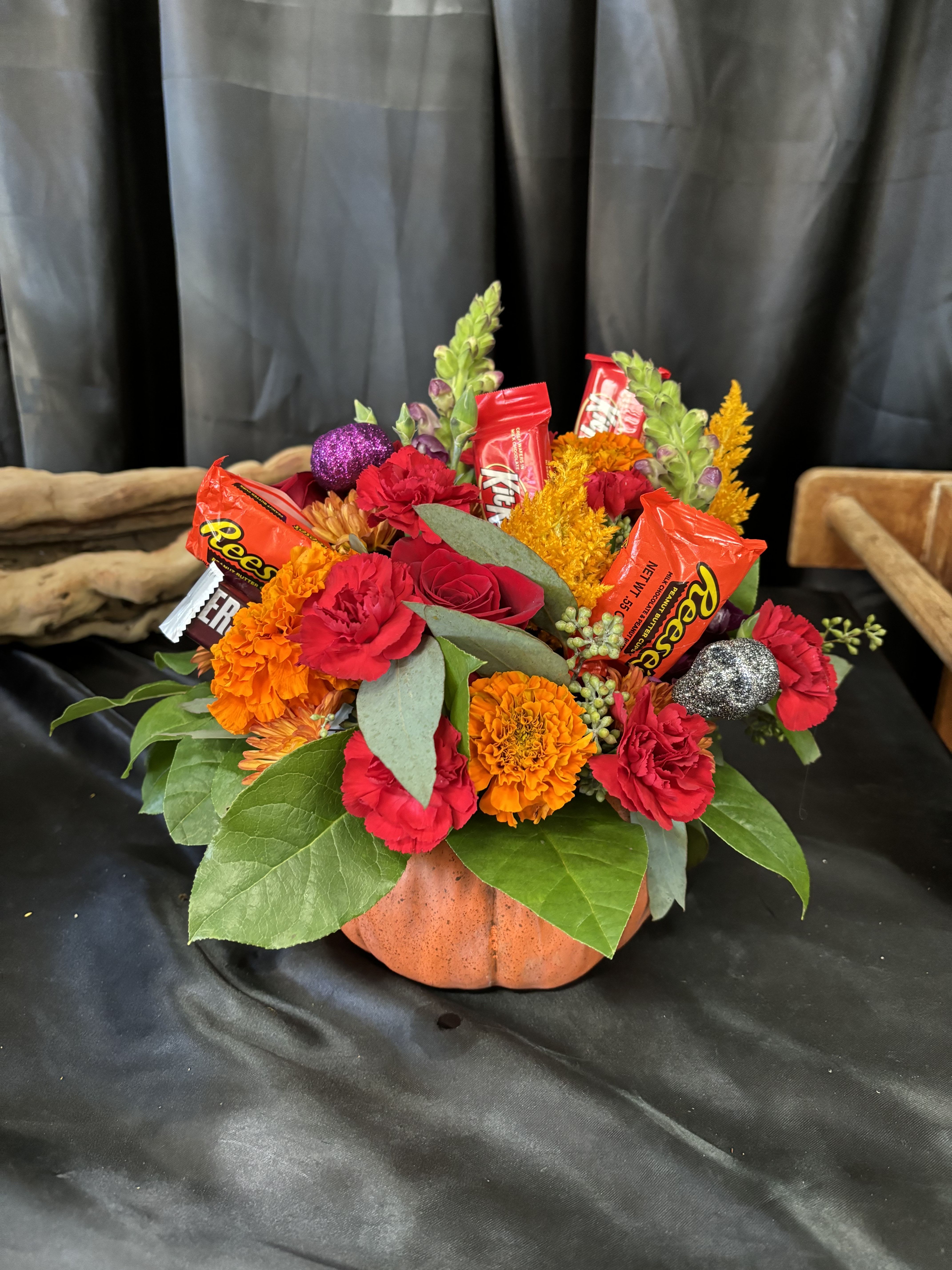Pumpkin-shaped floral arrangement with candy bars and bright flowers