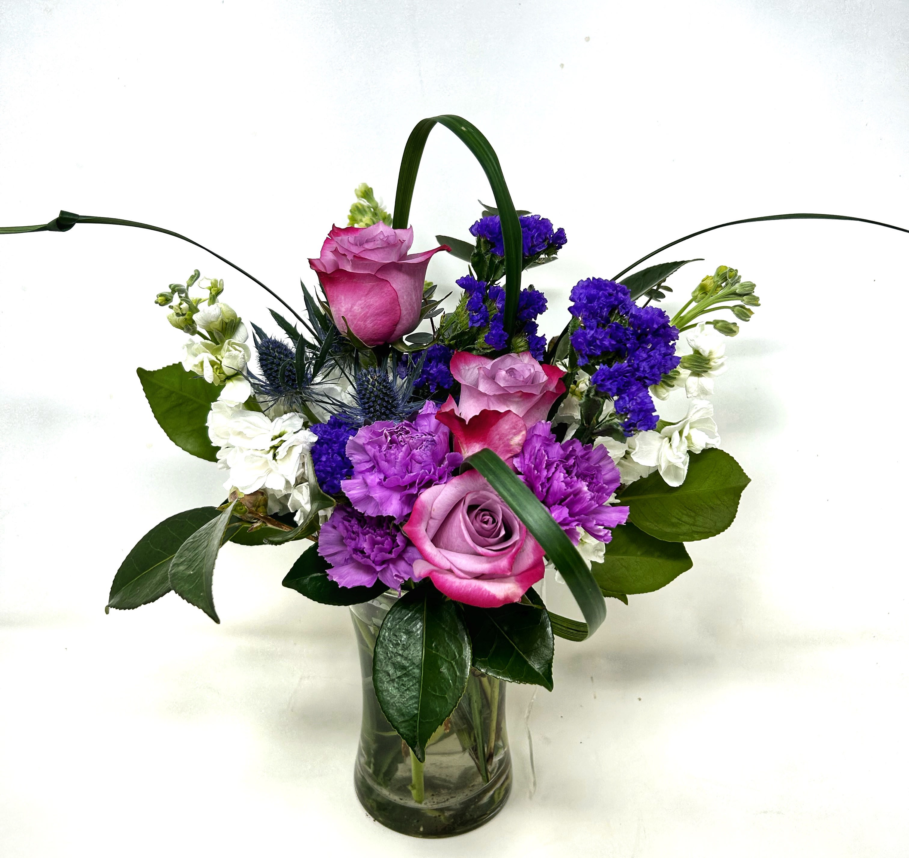 Pink and purple roses with white and blue flowers in a glass vase
