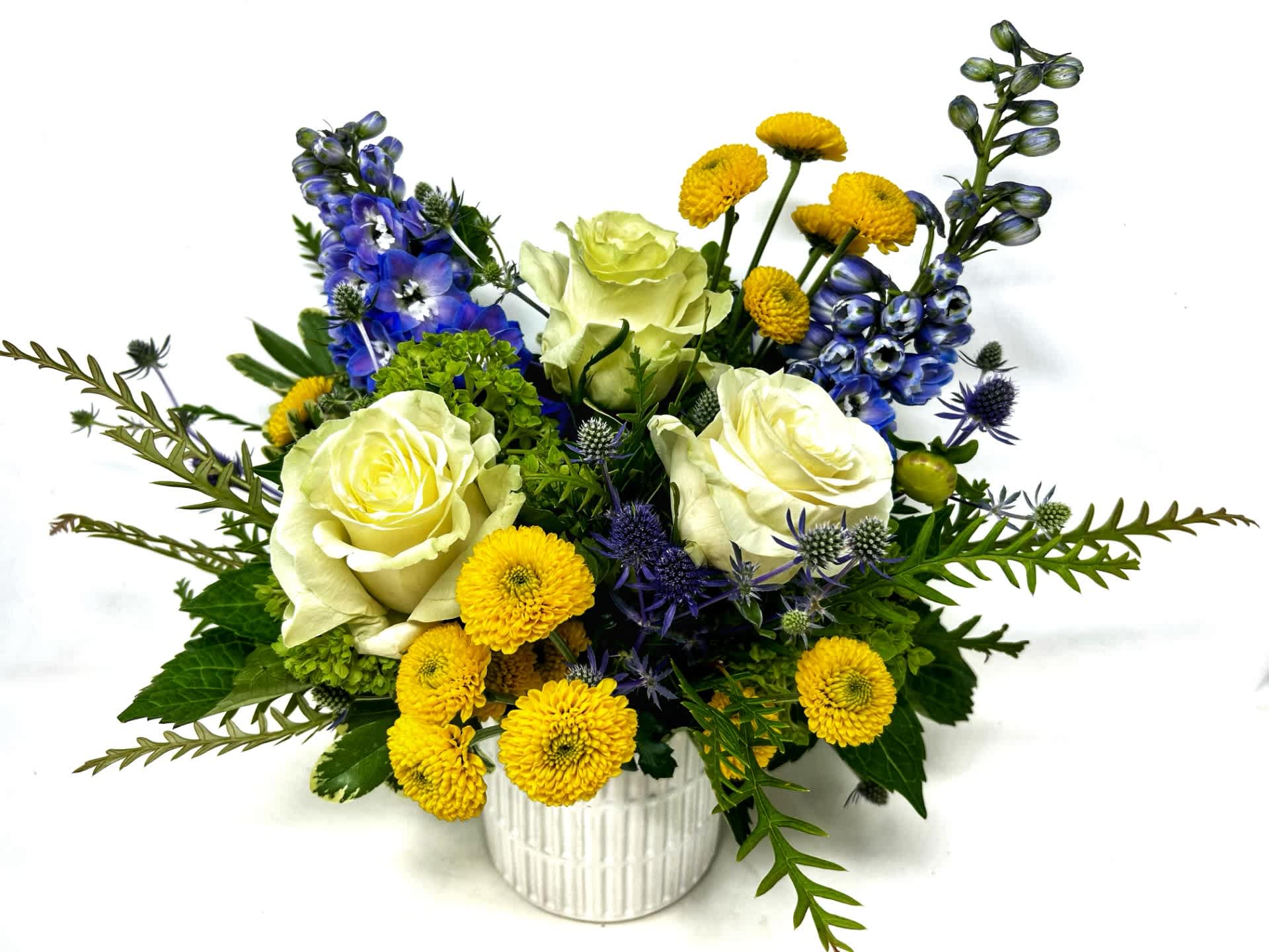 White roses, yellow pom flowers, and blue blooms in a white vase
