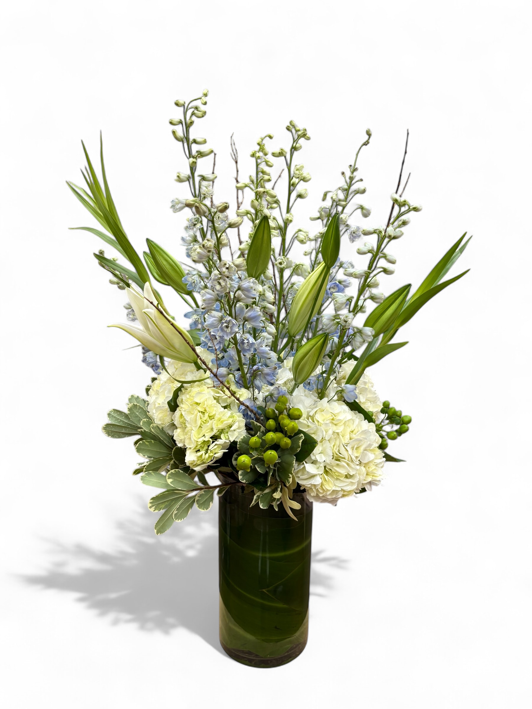 Tall white and pale blue floral arrangement in a dark glass vase