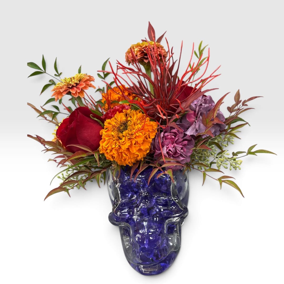 Colorful bouquet in a blue glass skull vase with roses and mums