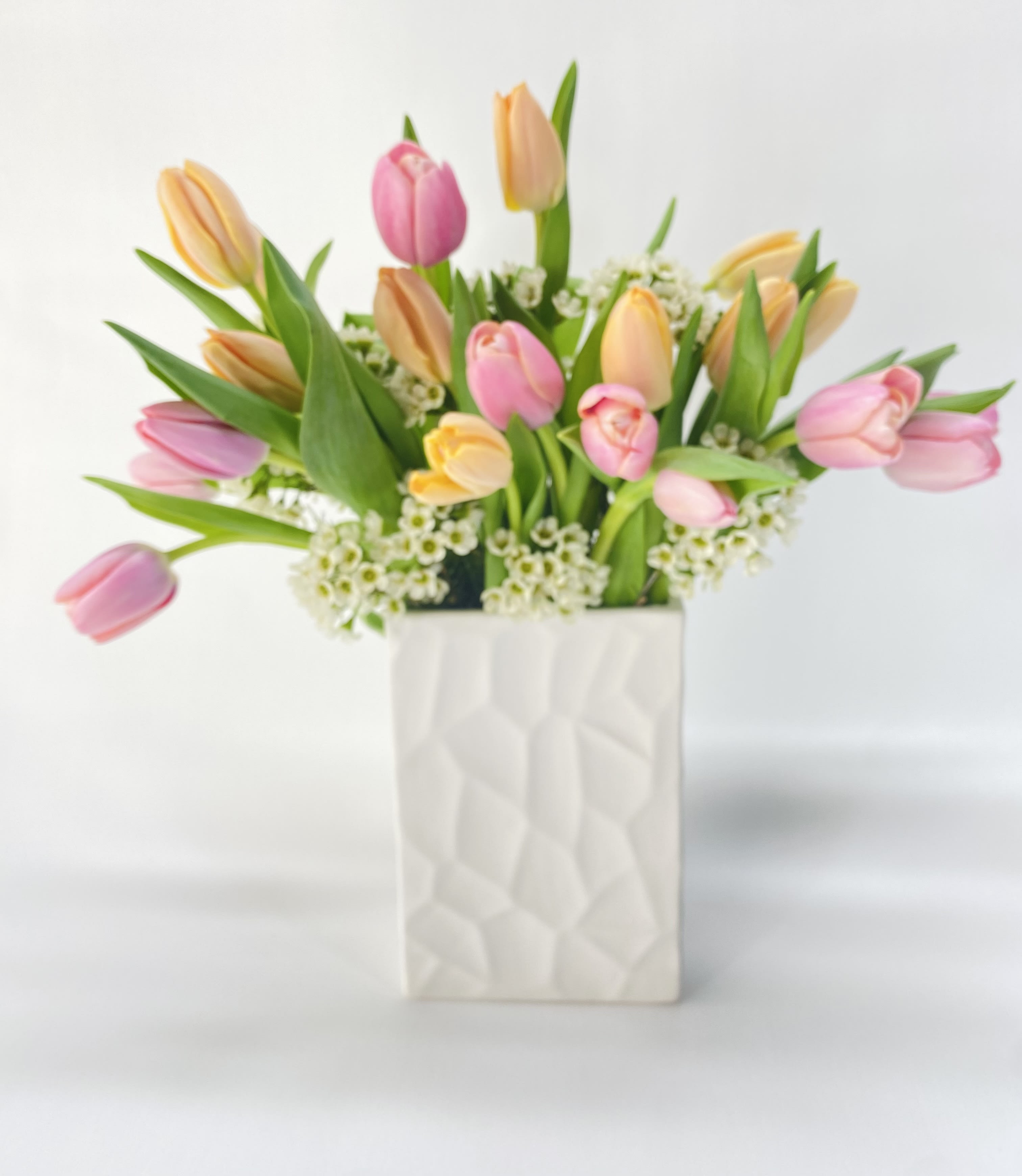 Pink and peach tulips arranged in a white textured vase