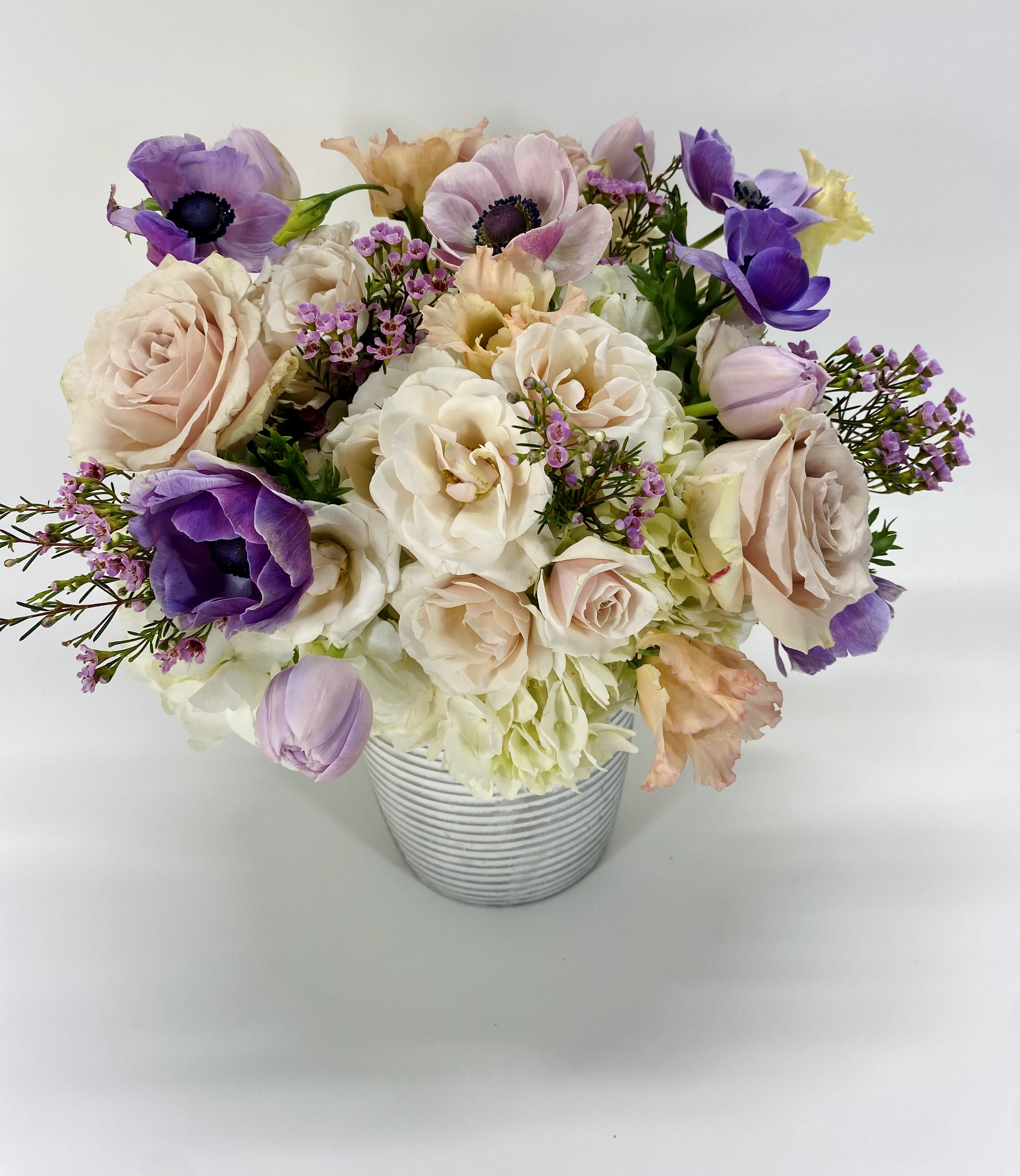Pastel bouquet of roses and purple anemones in a striped vase