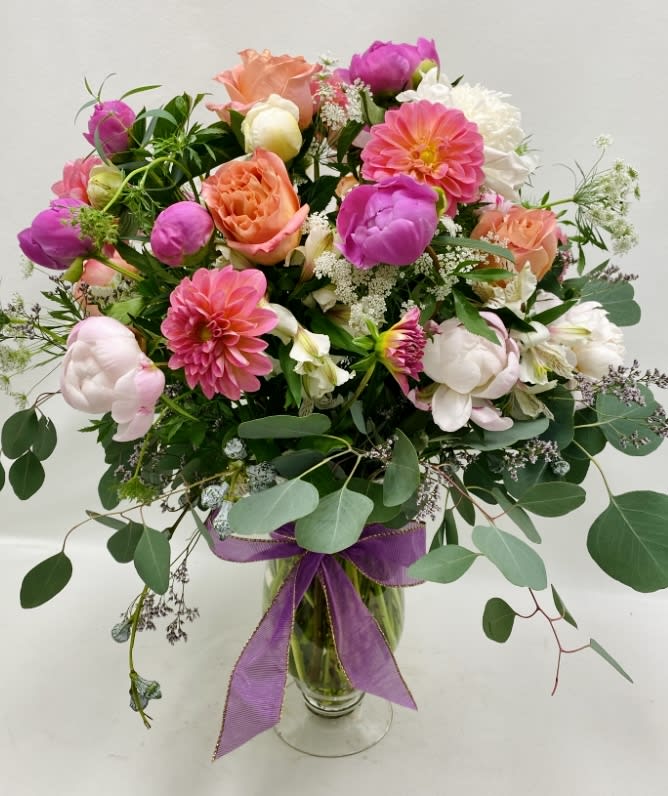 Mixed pink and peach bouquet in a glass vase with a purple ribbon