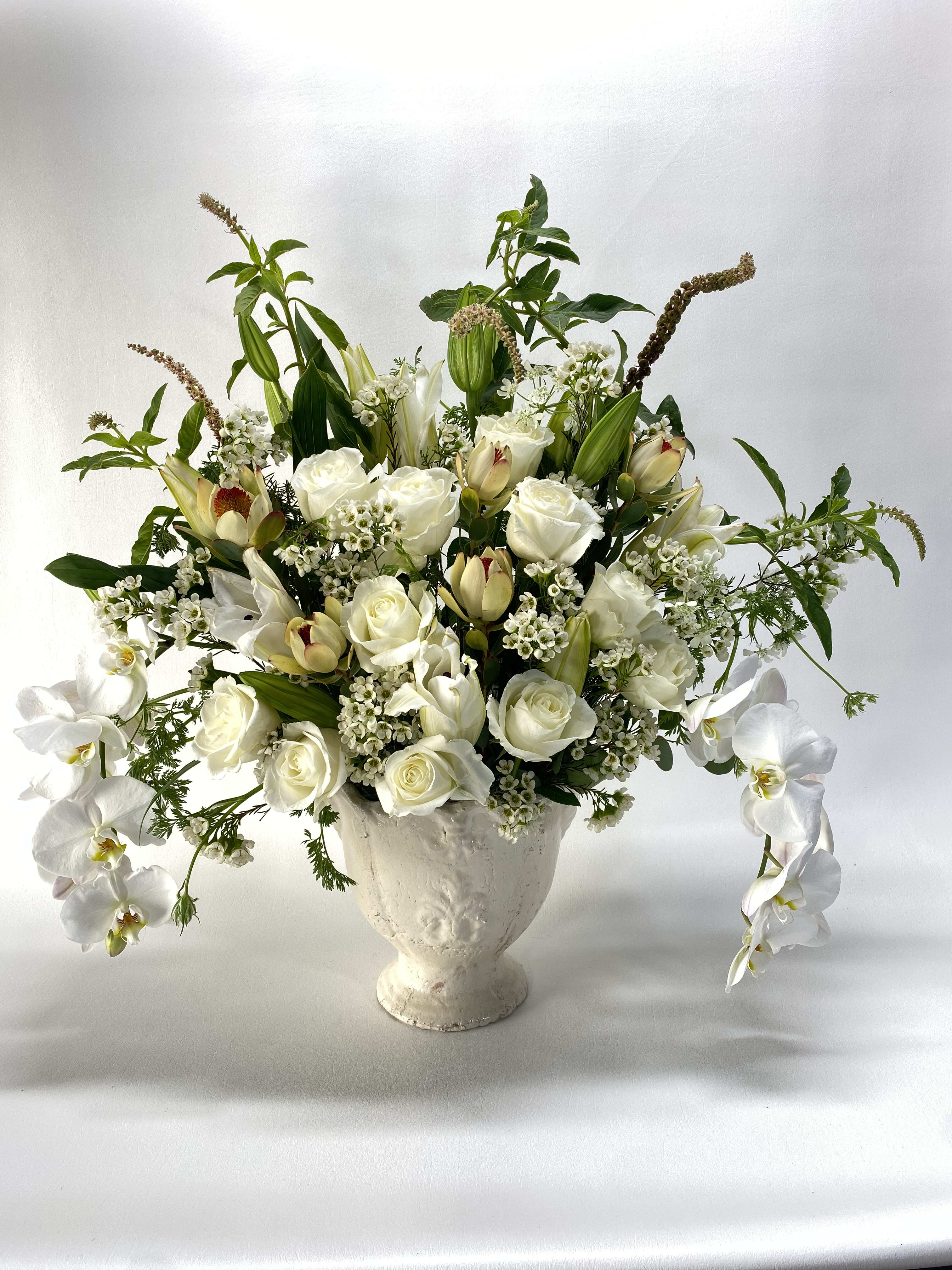 White roses and orchids arranged in a white urn vase