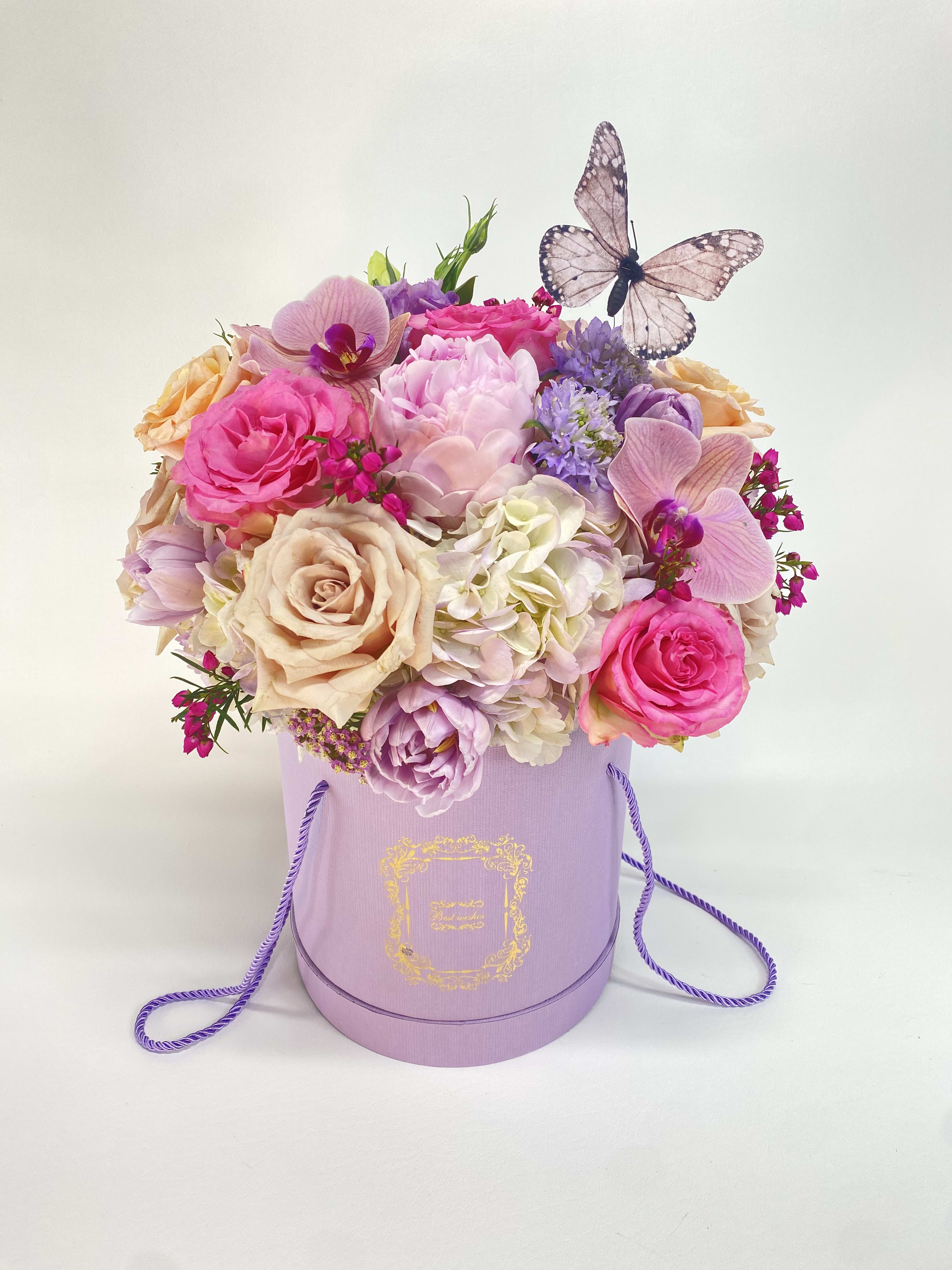 Pink and lavender flower arrangement in a lavender hat box with a butterfly topper