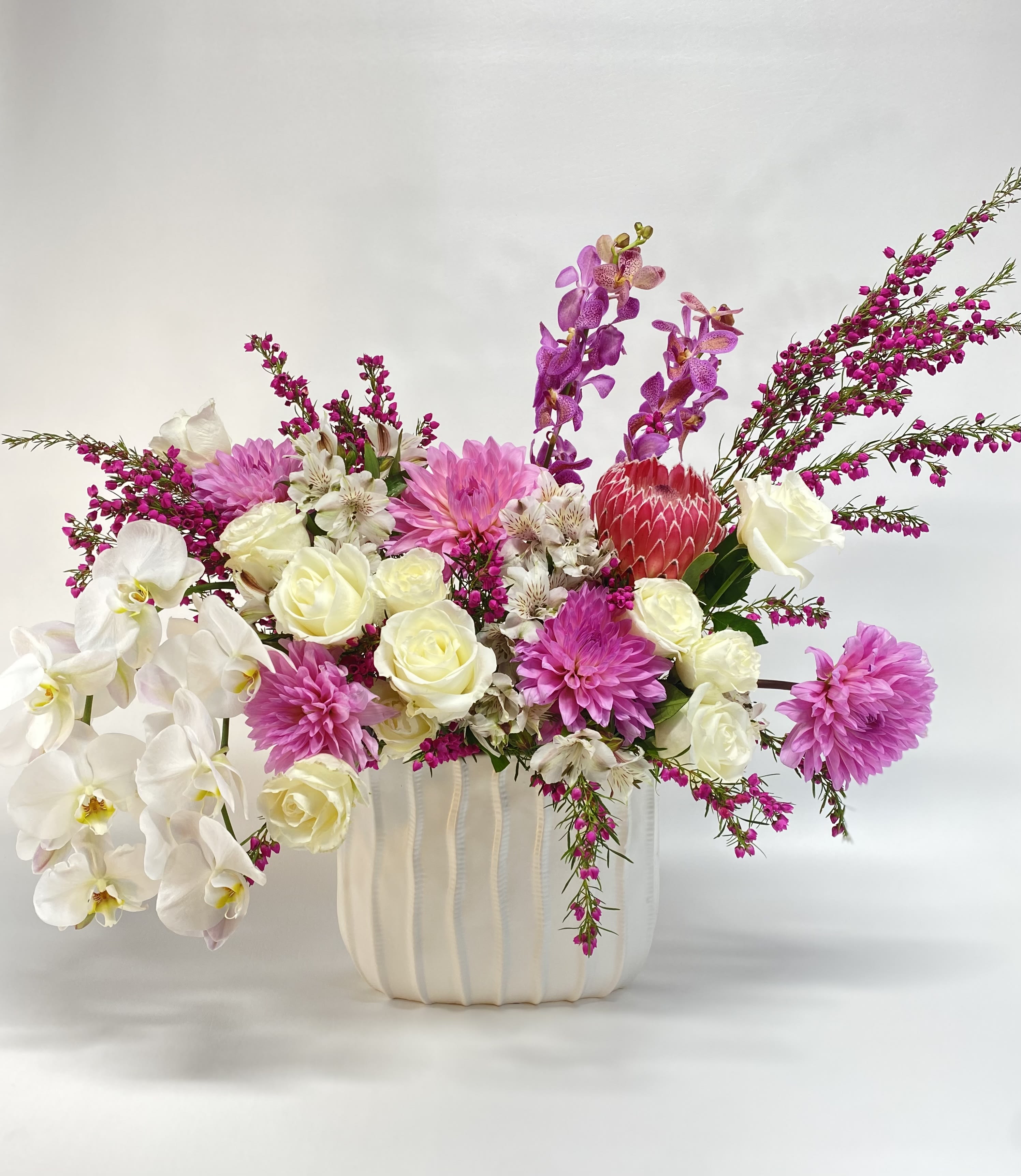 Mixed bouquet of white orchids, cream roses, pink dahlias, and purple orchids in a white vase