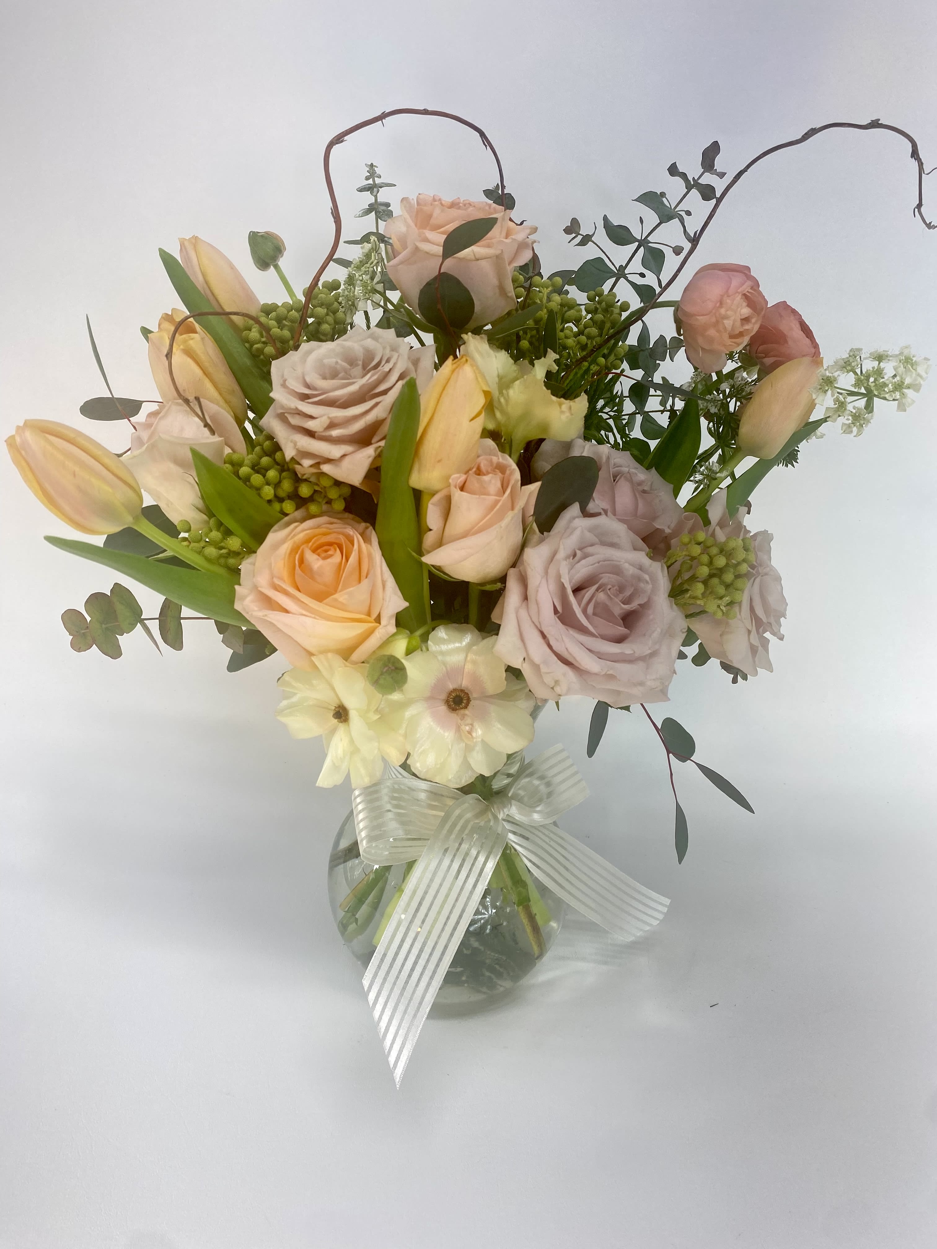 Mixed pastel roses and tulips in a clear glass vase with a ribbon