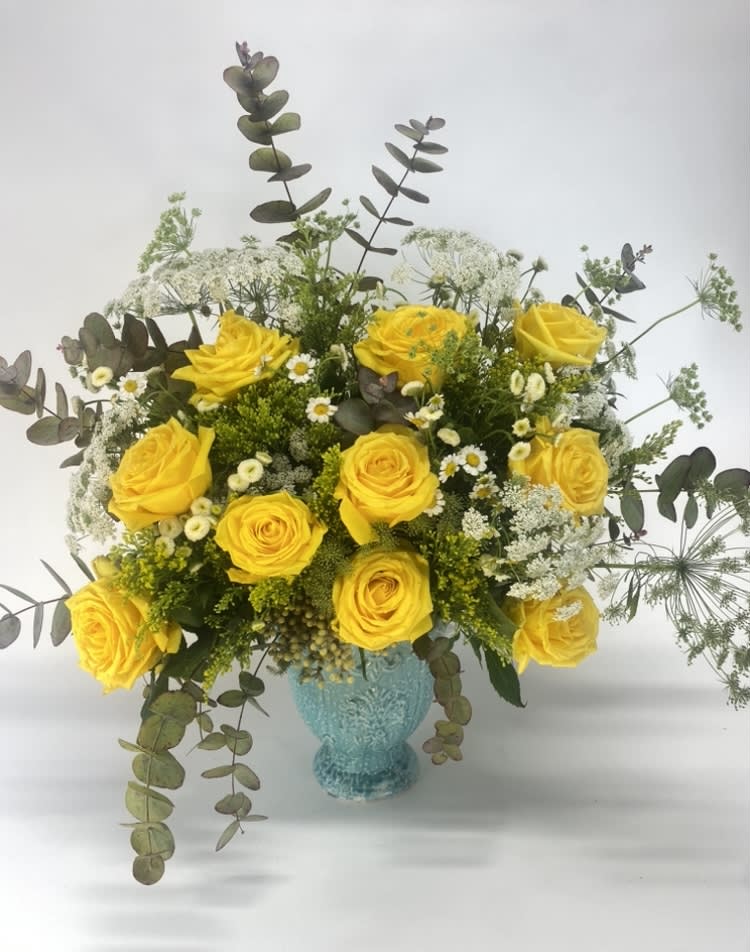 Yellow roses in a turquoise vase with airy white filler flowers