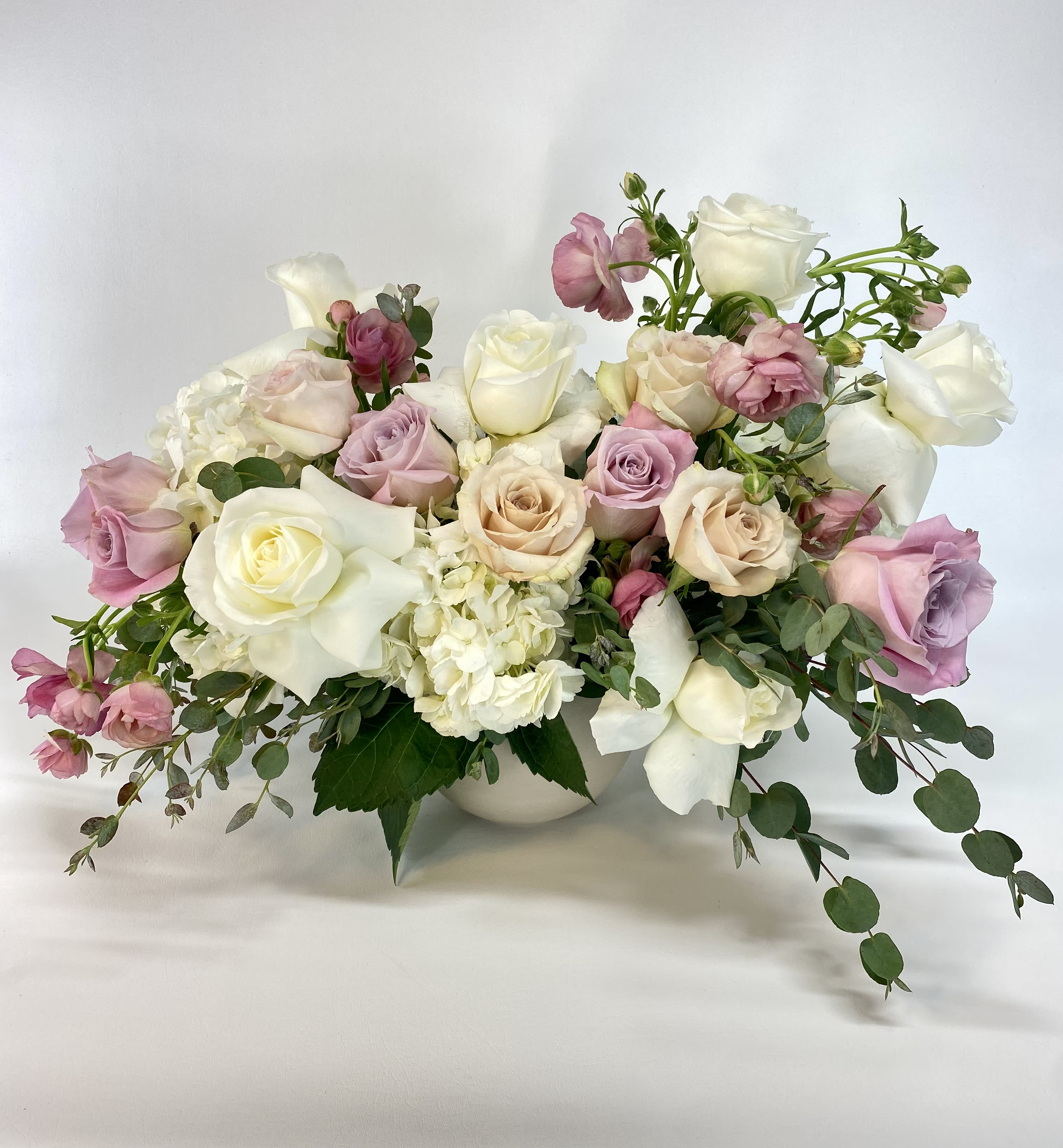 Pastel rose bouquet in a white vase with trailing greenery