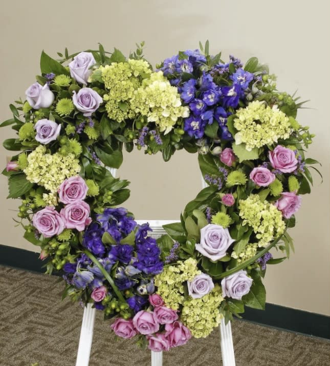 Heart-shaped floral wreath with purple, pink, and green flowers on a stand