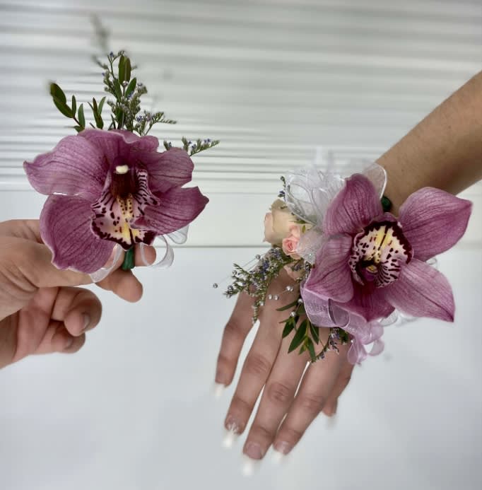 Two purple orchid wrist corsages held in hands.