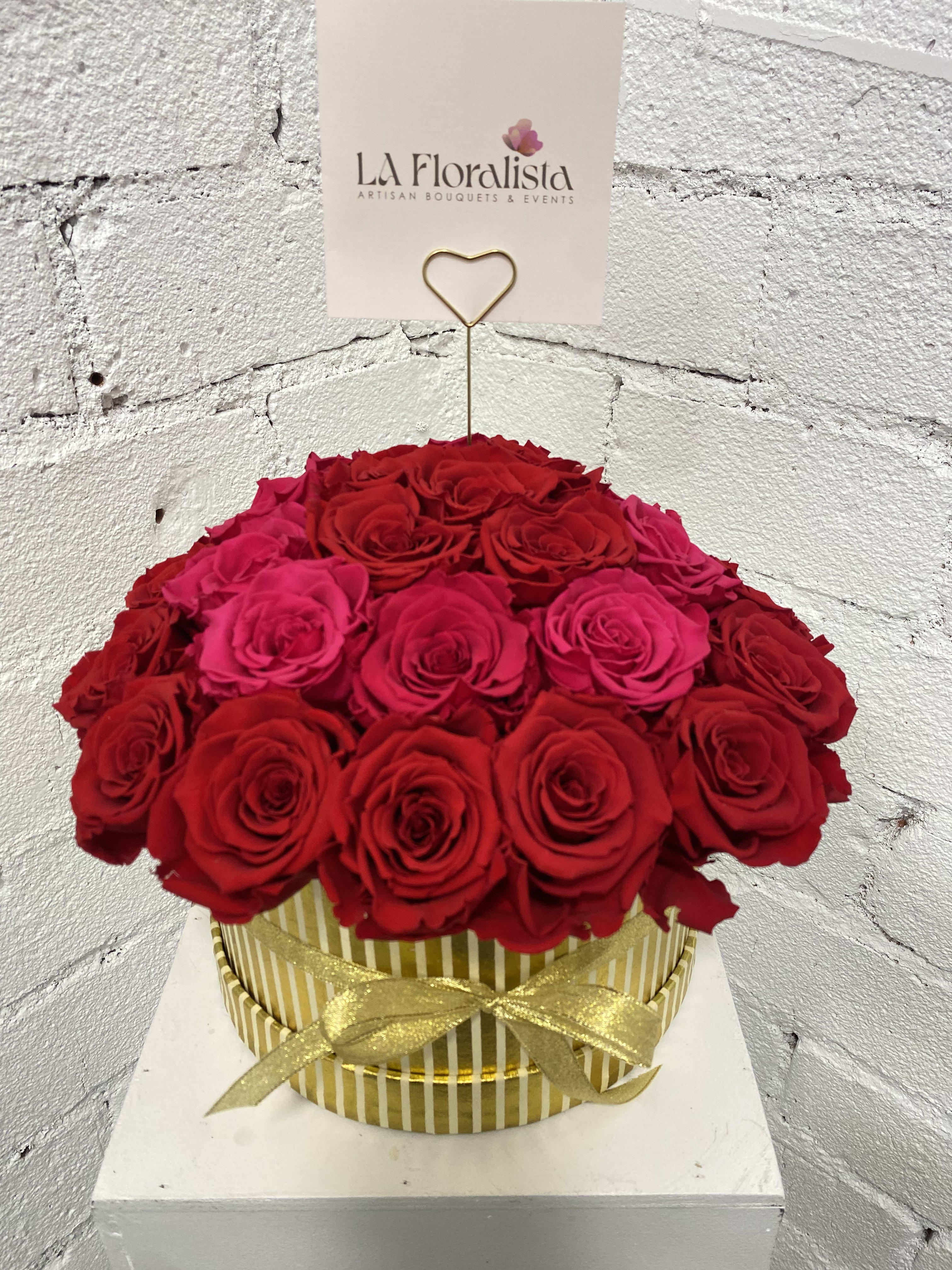 Round box of red and pink roses with a gold ribbon and card holder