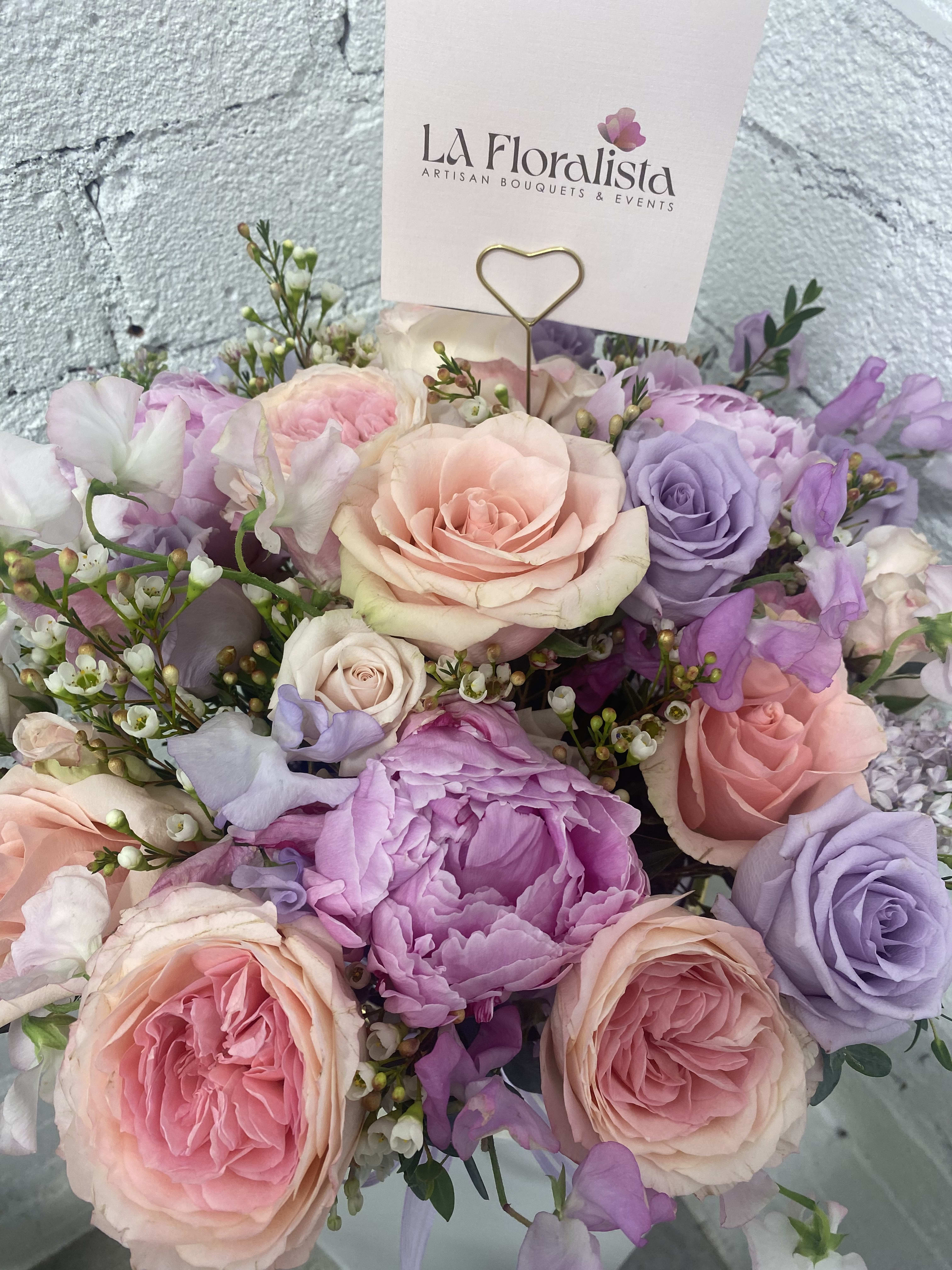 Pastel bouquet of roses and purple blooms with a florist card