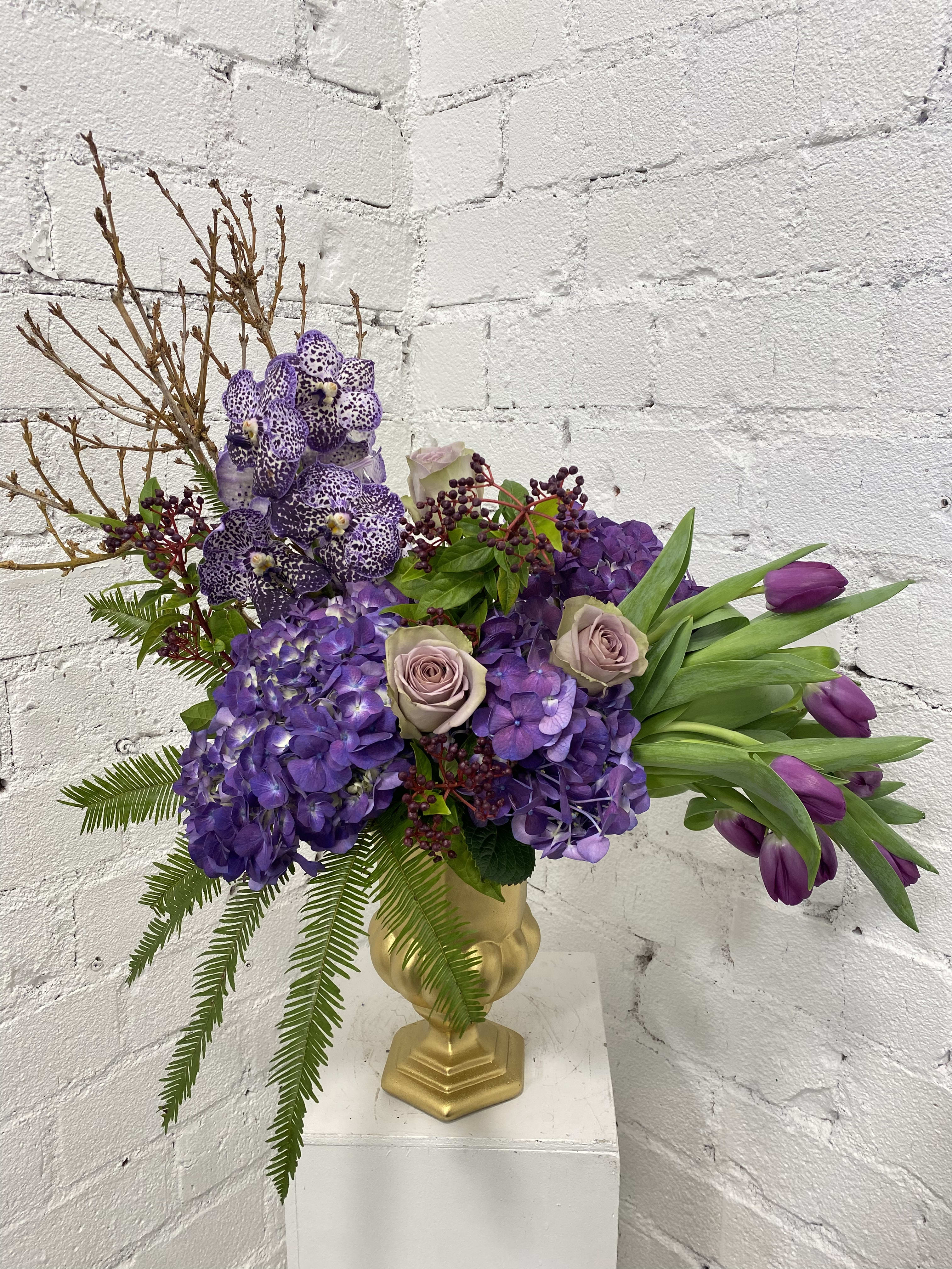 Purple floral arrangement in a gold vase with tulips and orchids