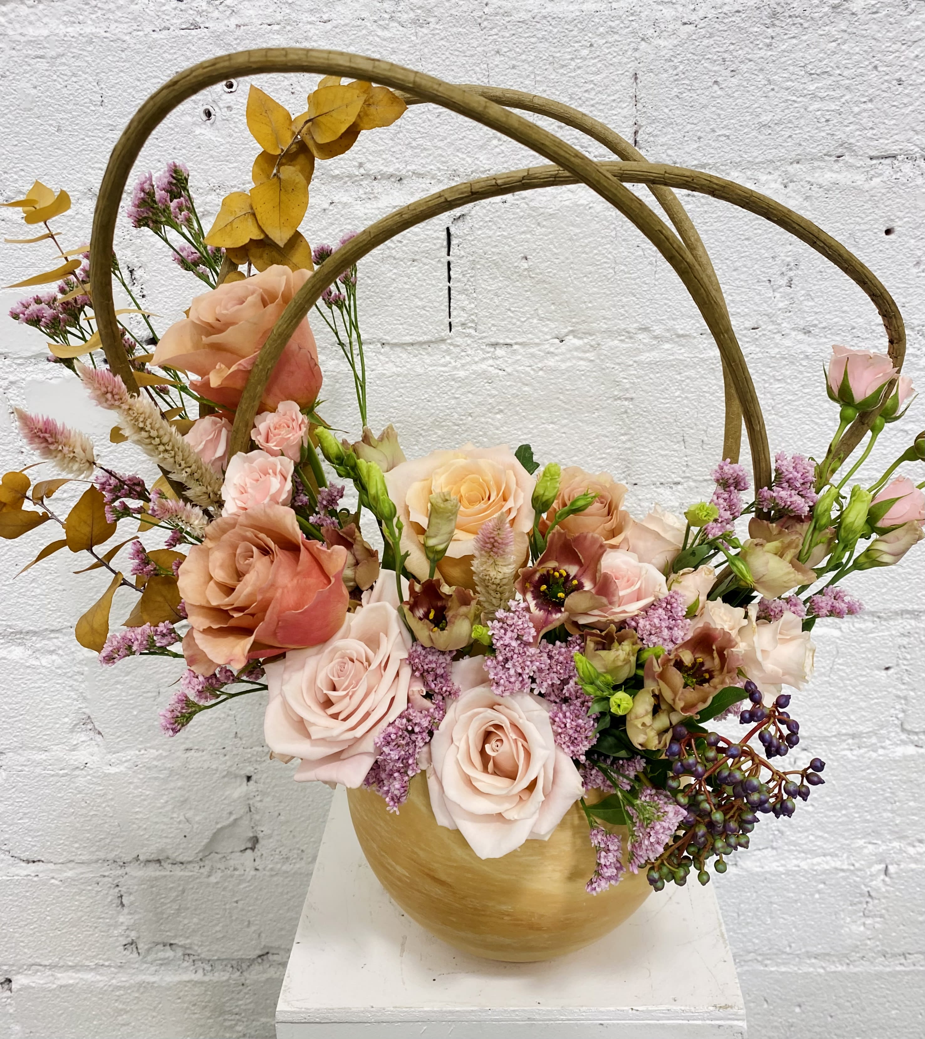 Basket arrangement of peach and pink roses with purple filler flowers