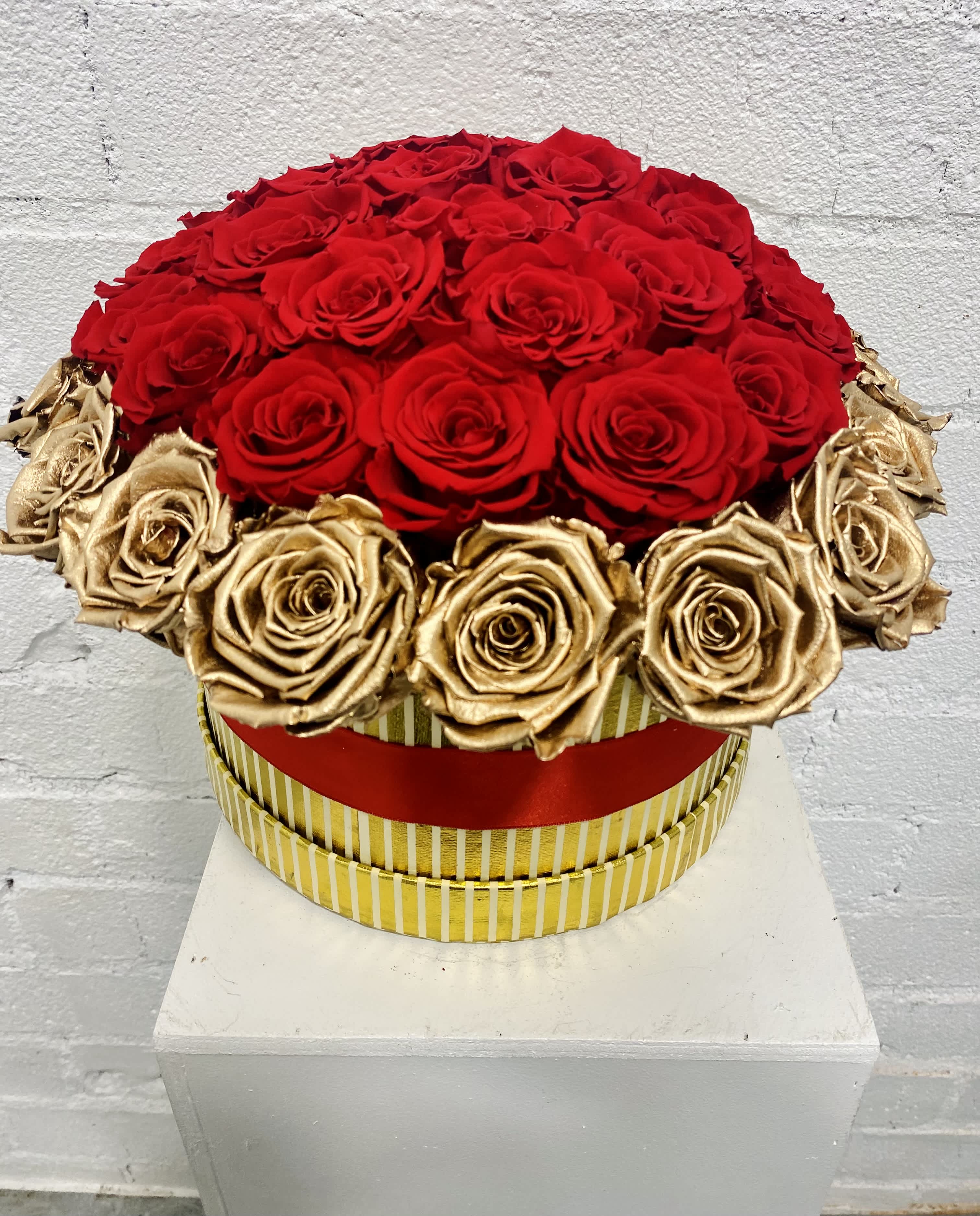Round arrangement of red and gold roses in a striped box