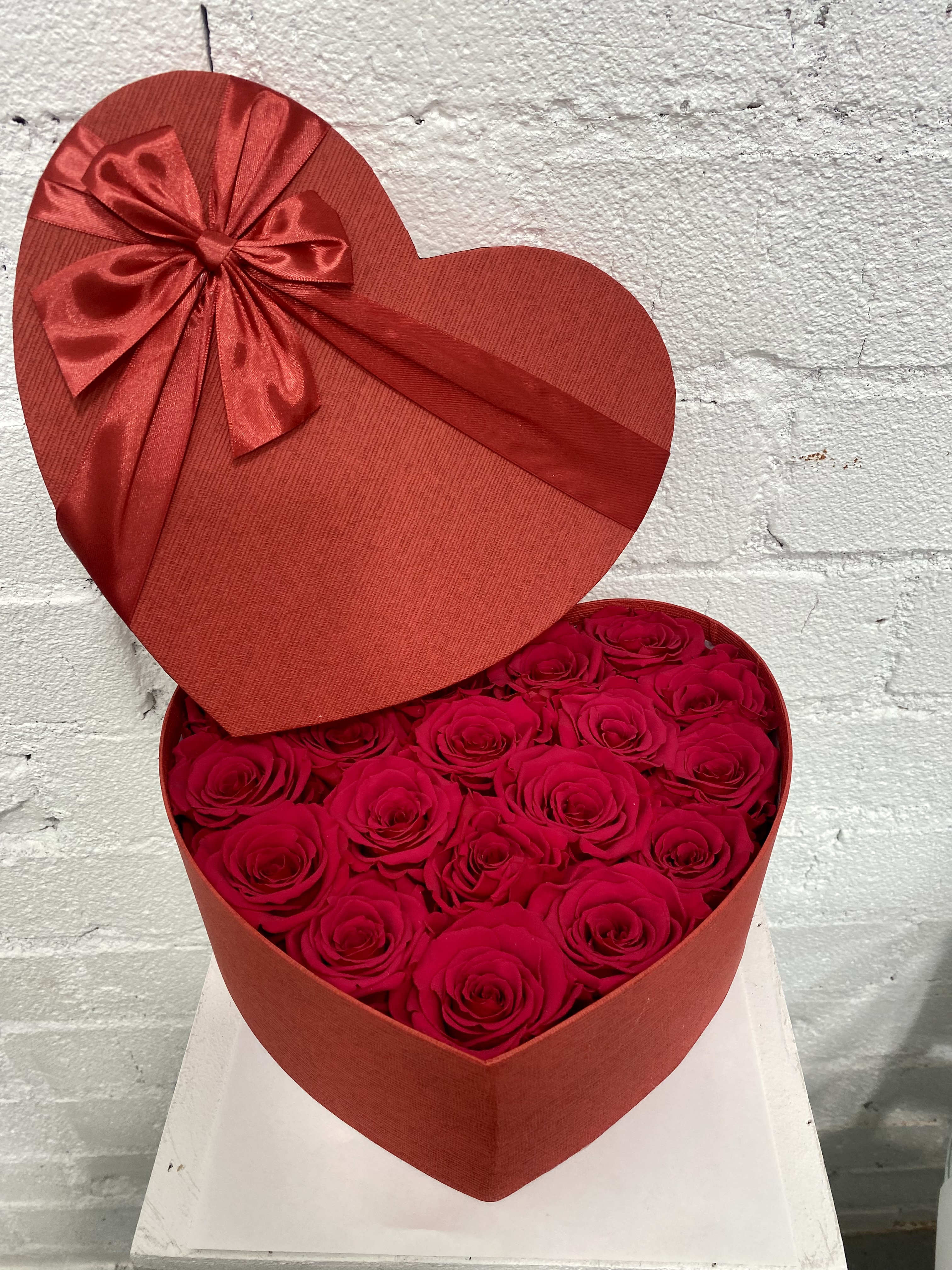Heart-shaped box filled with red roses and topped with a red ribbon bow