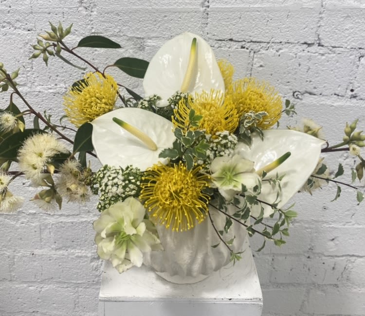 White anthuriums and yellow pincushion blooms in a white vase