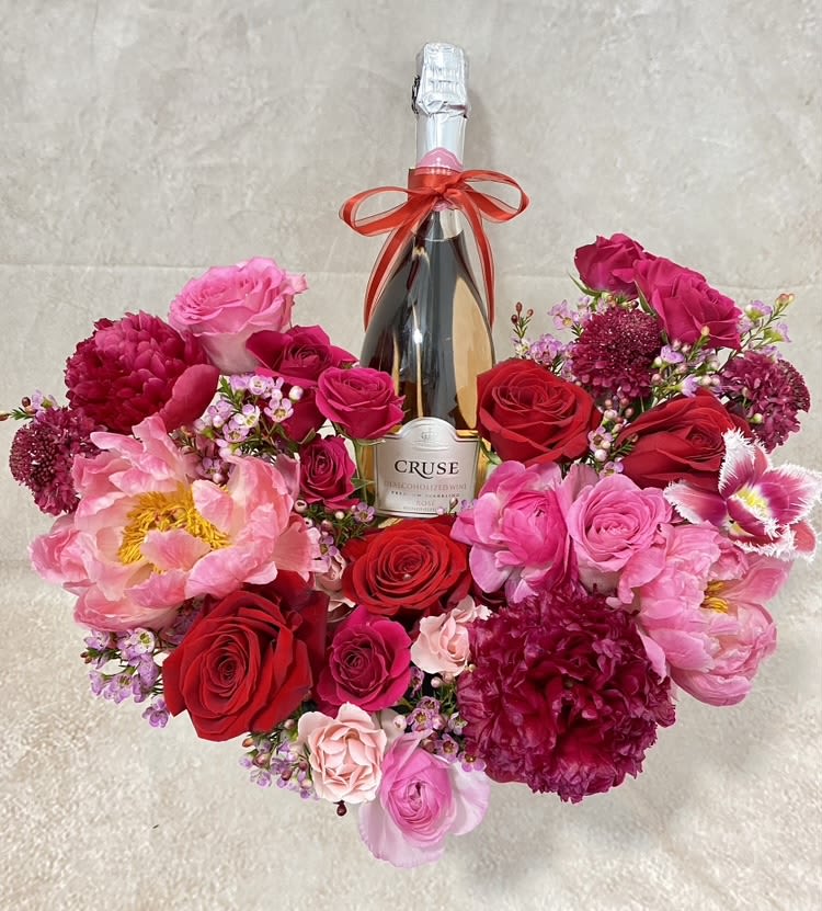 Heart-shaped bouquet of pink and red flowers around a champagne bottle