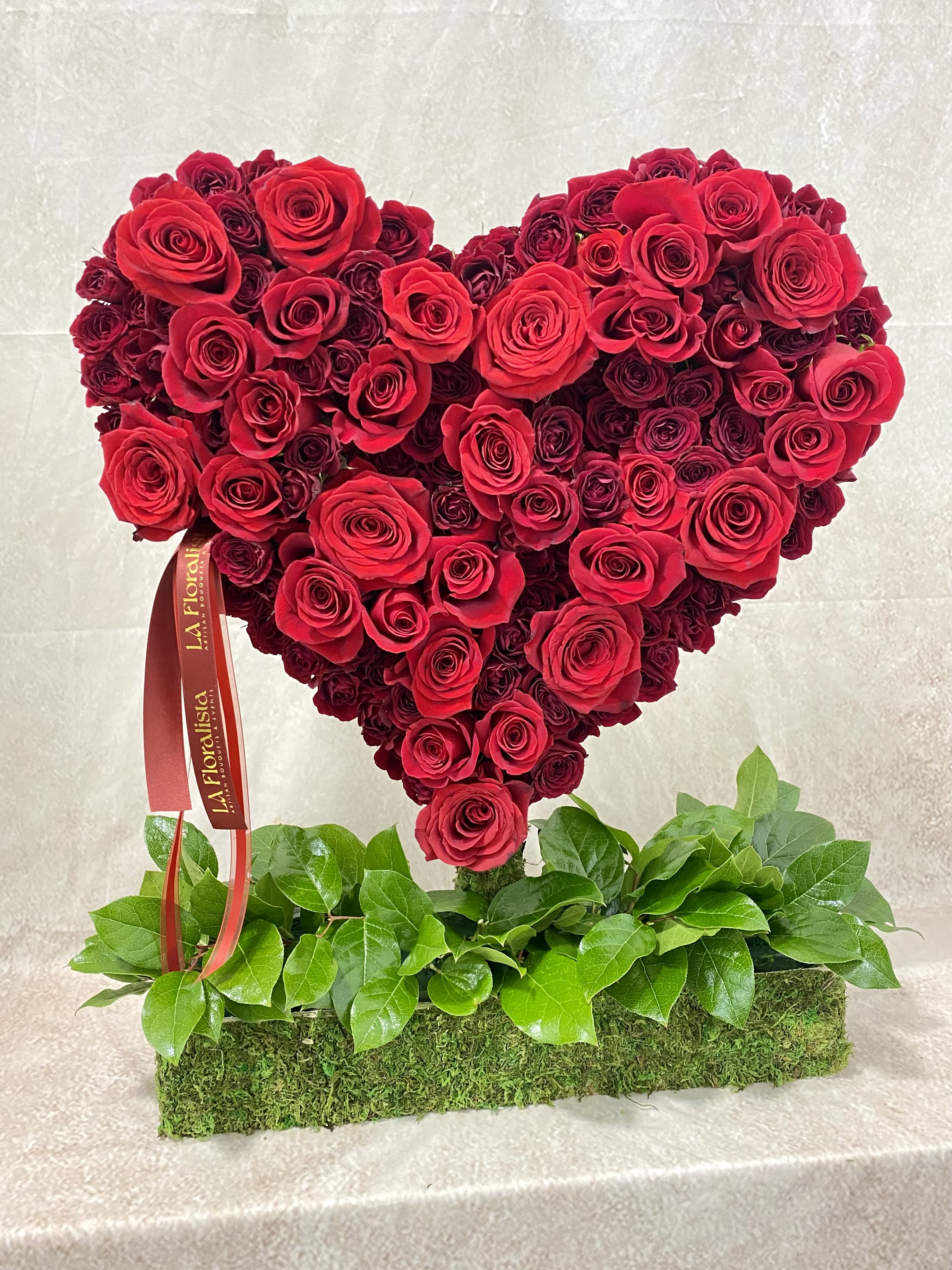 Heart-shaped red rose arrangement on a moss-covered base