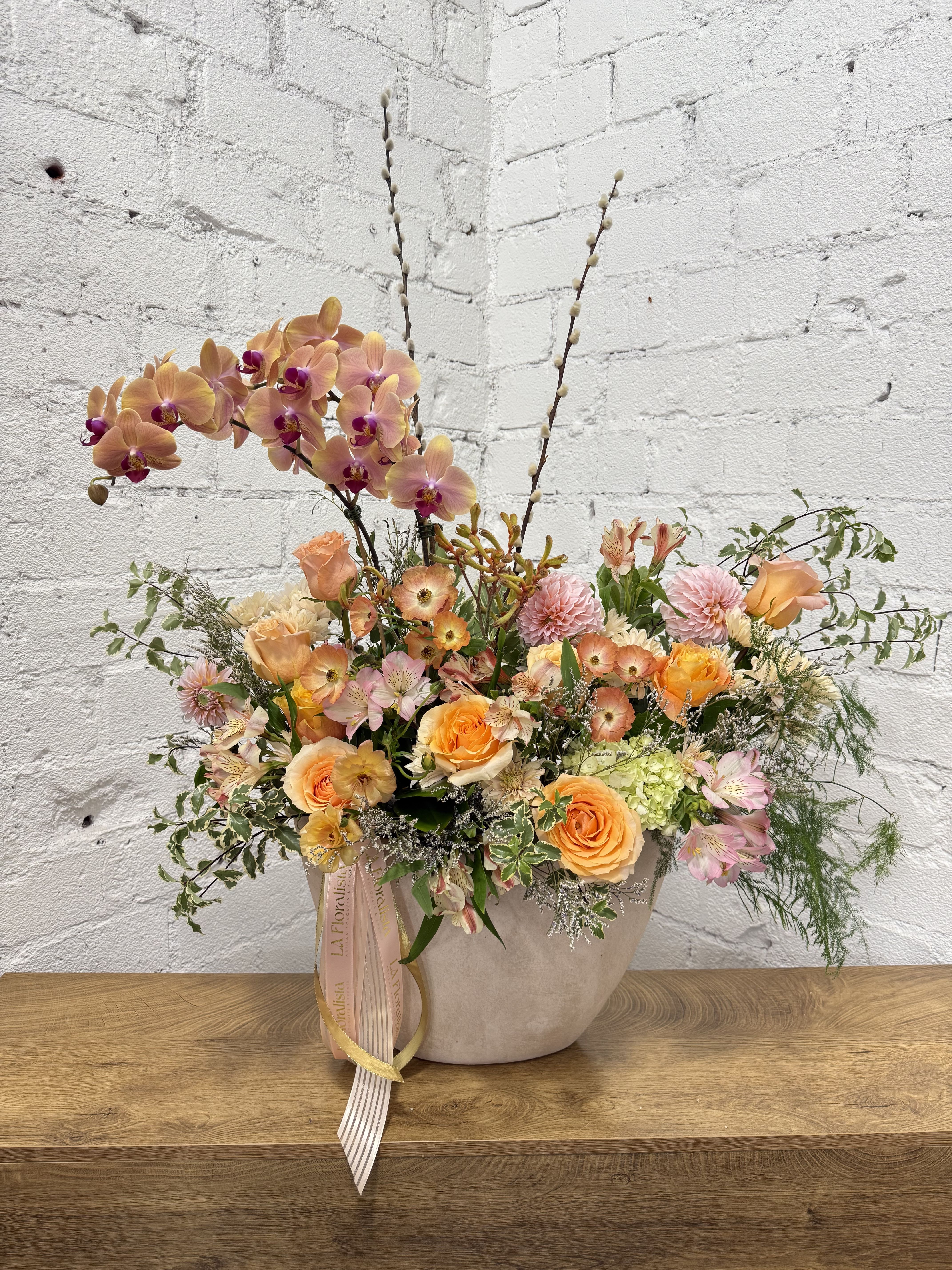 Peach and pink floral arrangement in a beige vase with tall orchid stems