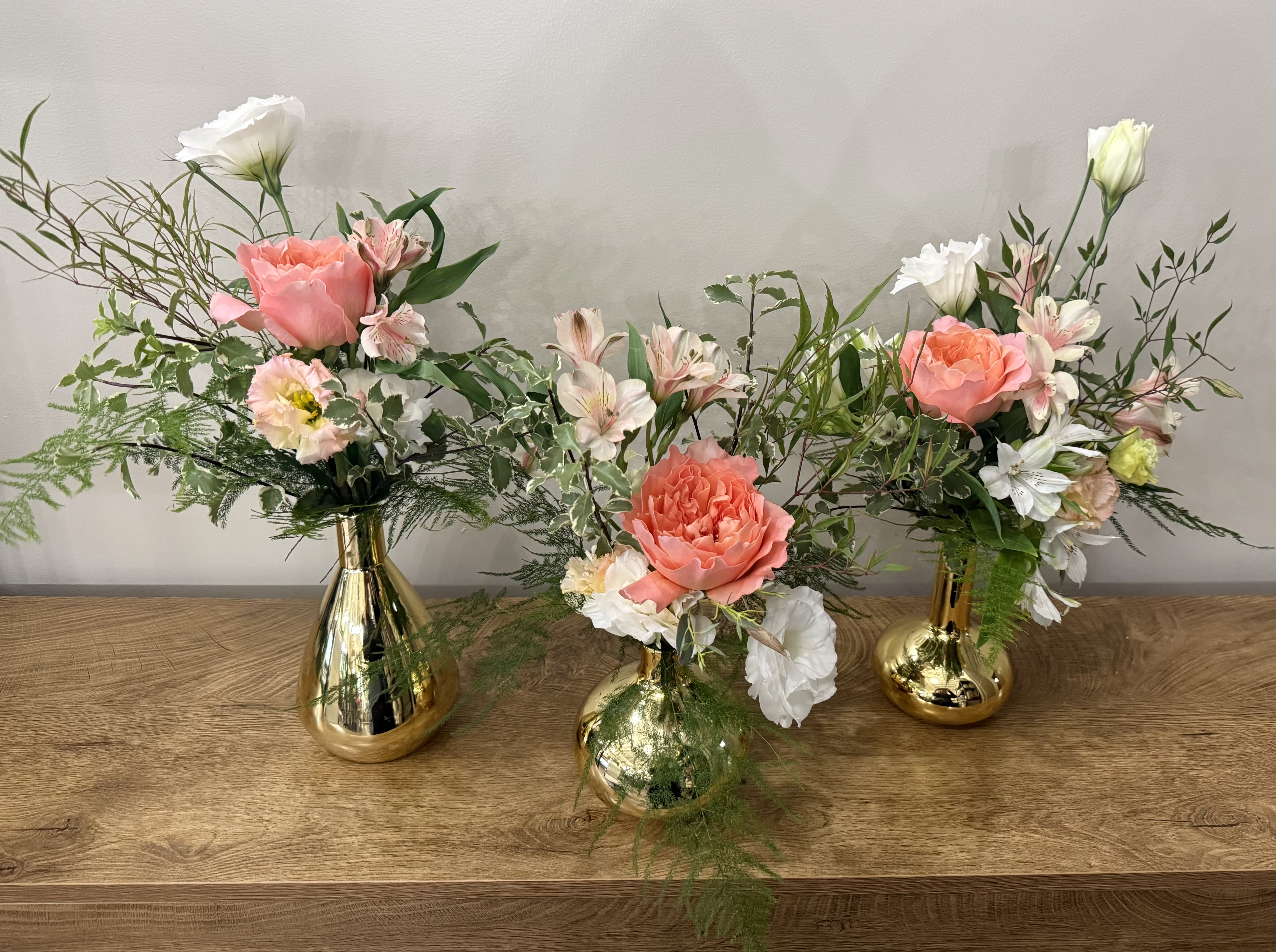 Three floral arrangements in gold vases with pink and white blooms