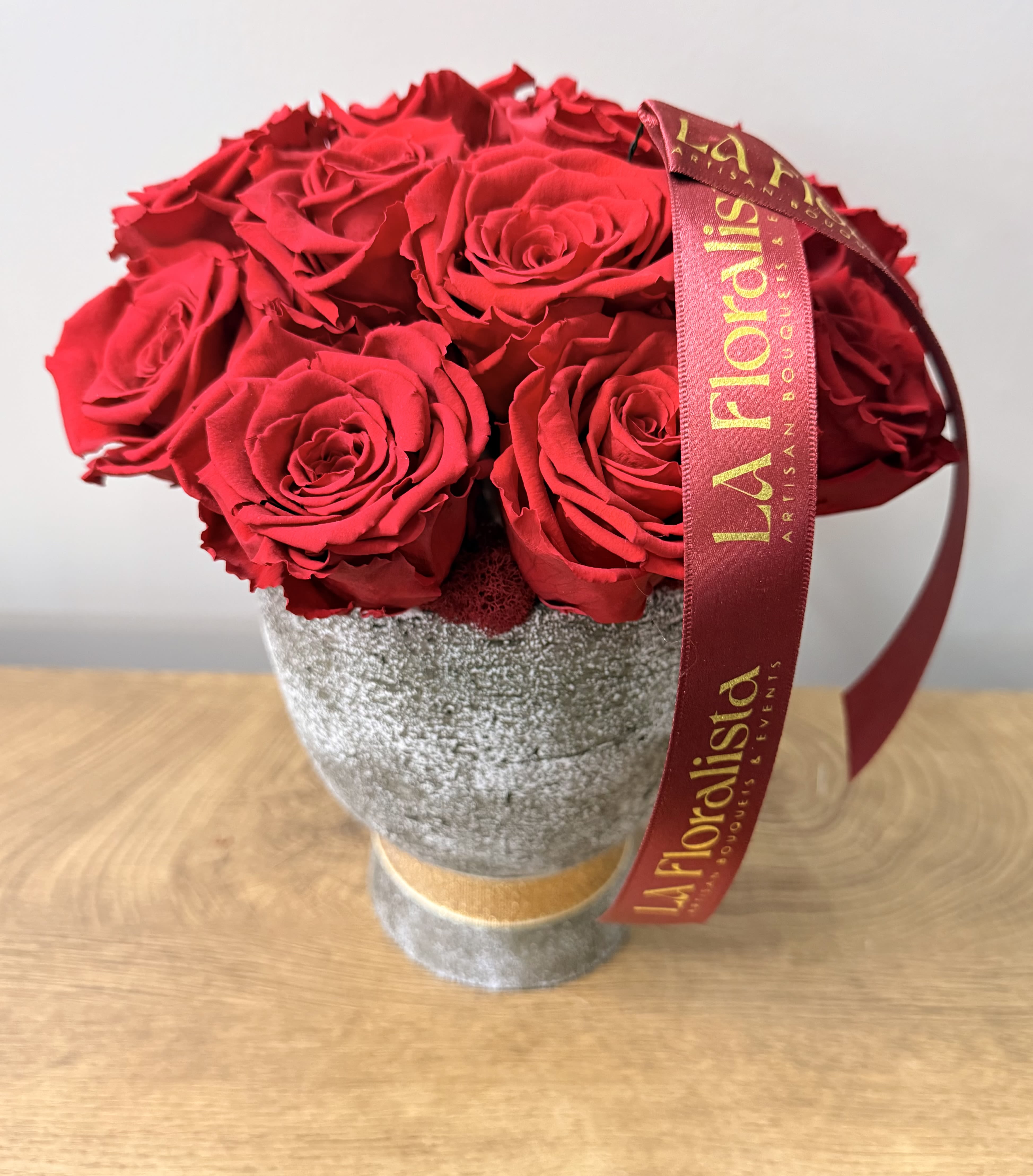 Red roses arranged in a gray textured vase with a burgundy ribbon