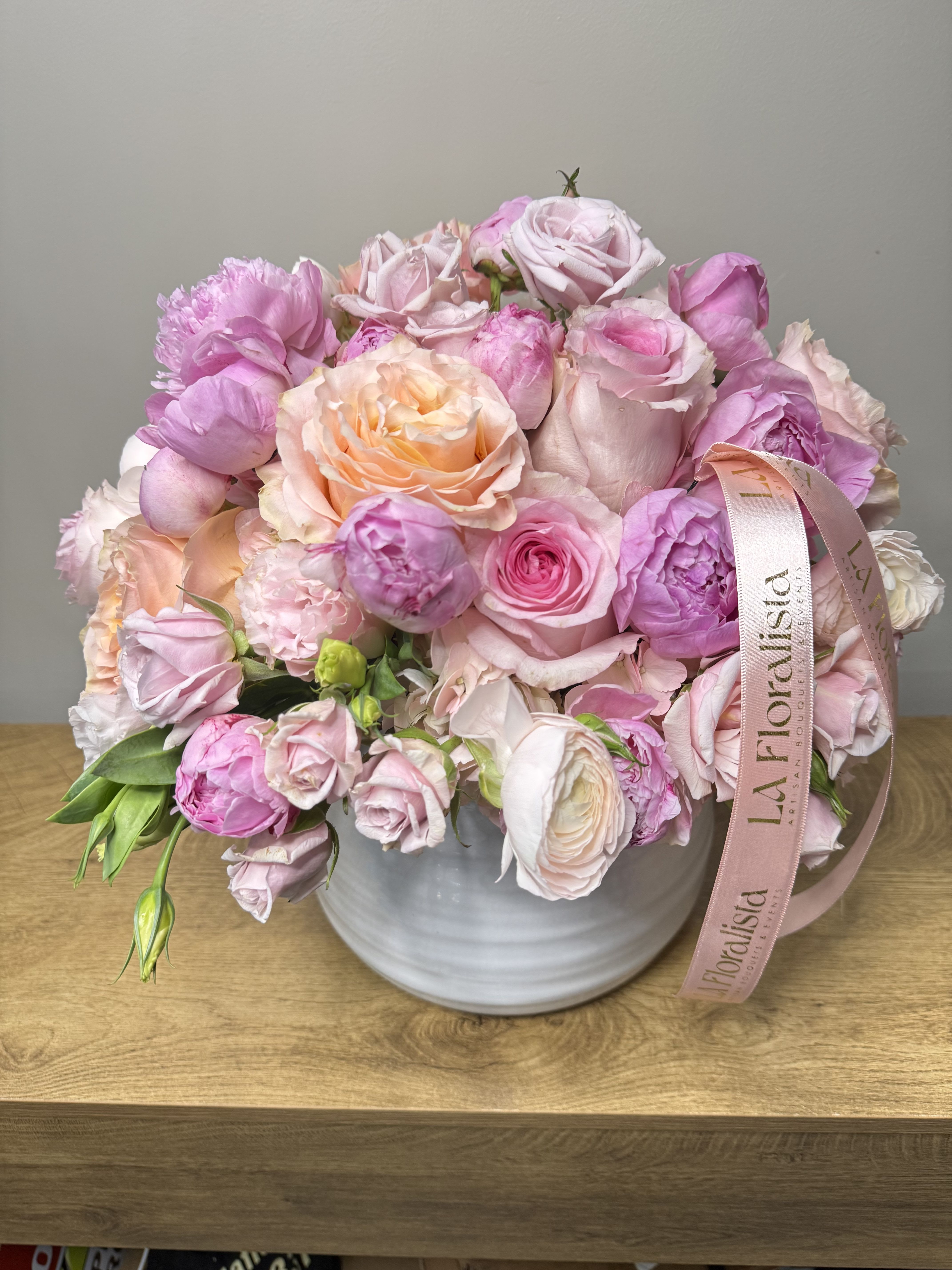 Pink and peach roses arranged in a white vase with a ribbon