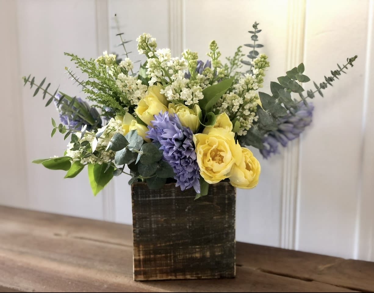 Yellow and lavender flowers arranged in a square wooden vase