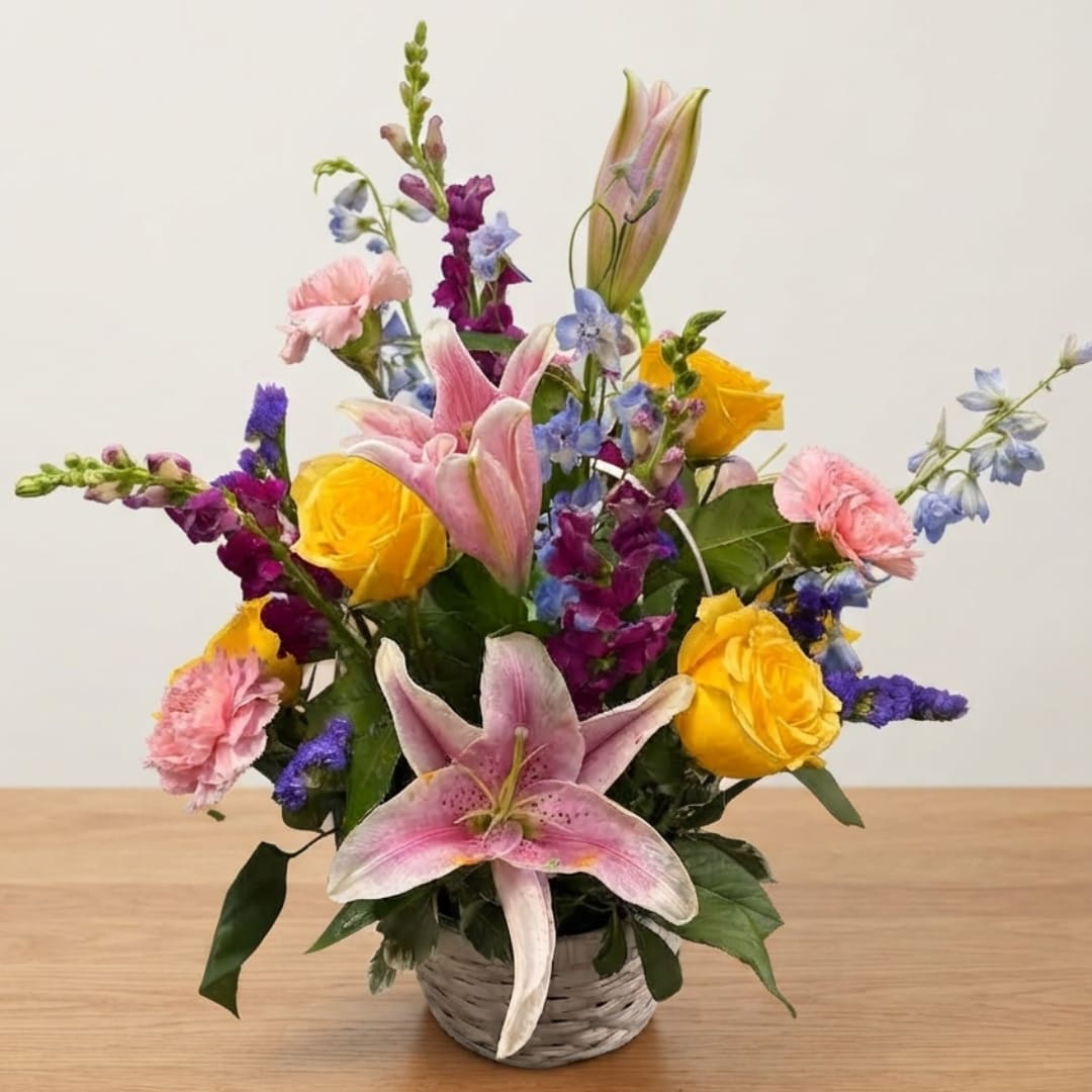 Mixed bouquet with pink lilies, yellow roses, and purple flowers in a woven basket