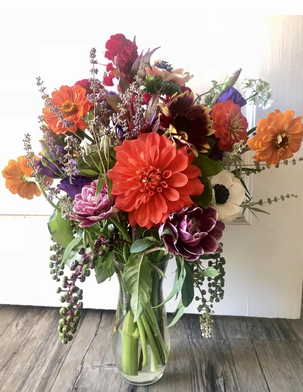 Tall mixed bouquet of orange, red, purple, and white flowers arranged in a clear glass vase.