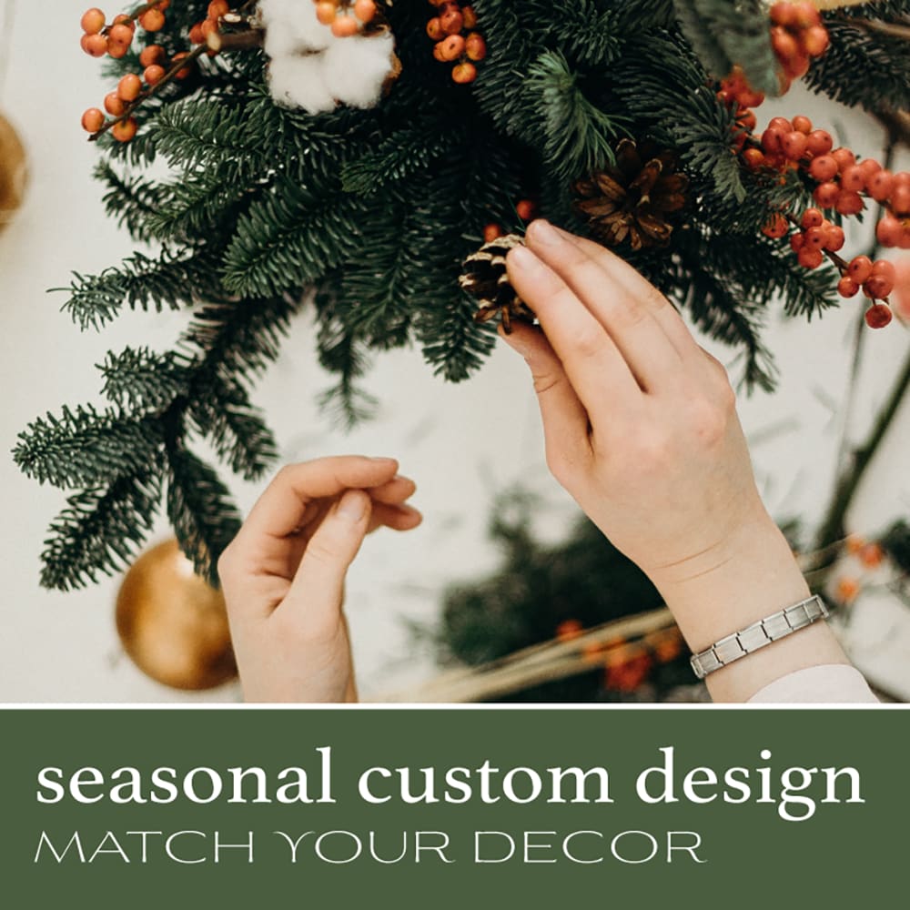 Hands decorating a holiday wreath with pinecones and red berries