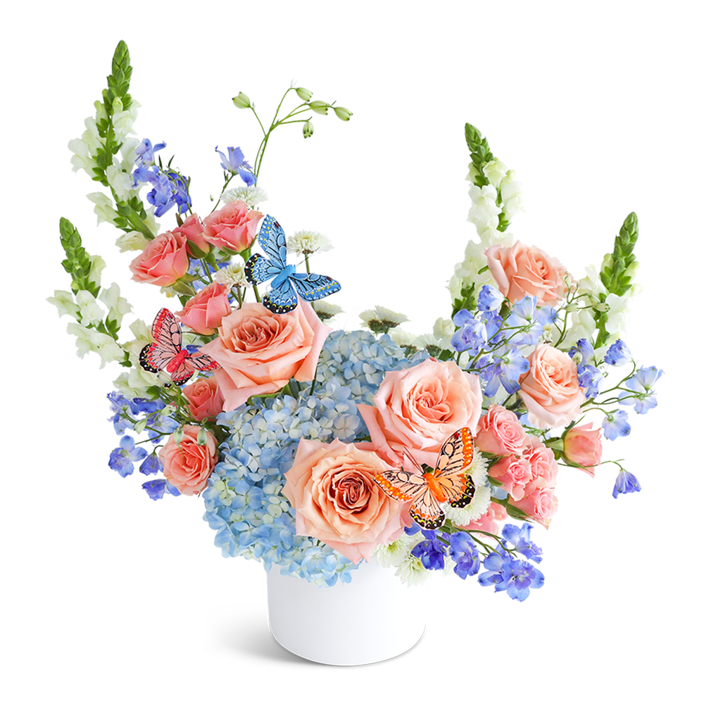 Peach roses and blue hydrangeas in a white vase with butterfly picks